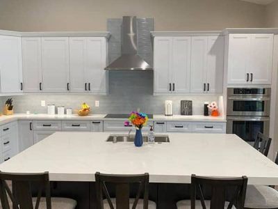 A kitchen with white cabinets and a large island with a vase of flowers on it.