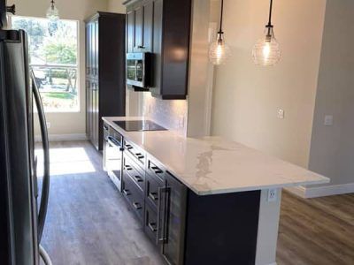 A kitchen with black cabinets , white counter tops , stainless steel appliances and a large island.