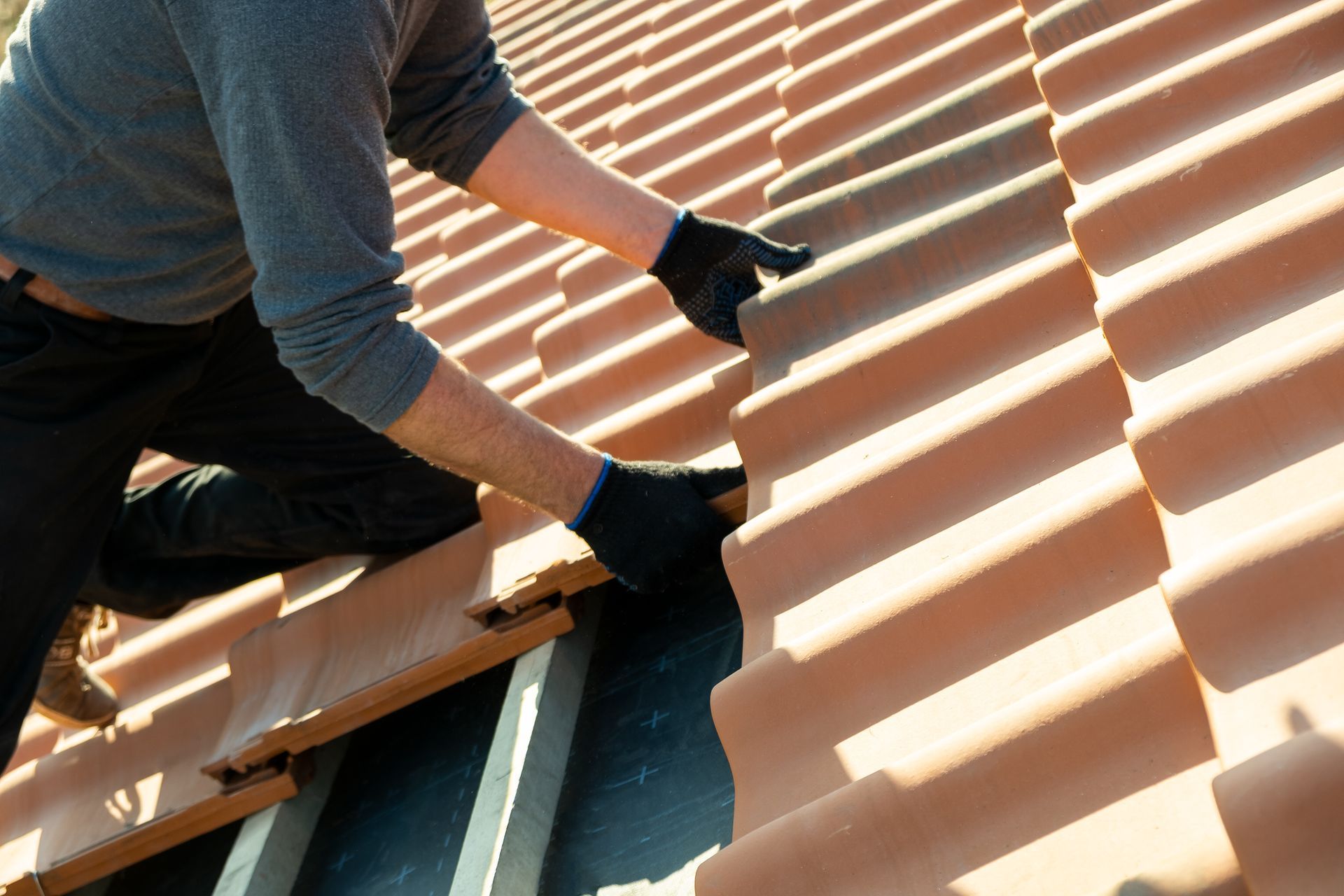 Person installing clay roof tiles on a sunny day.