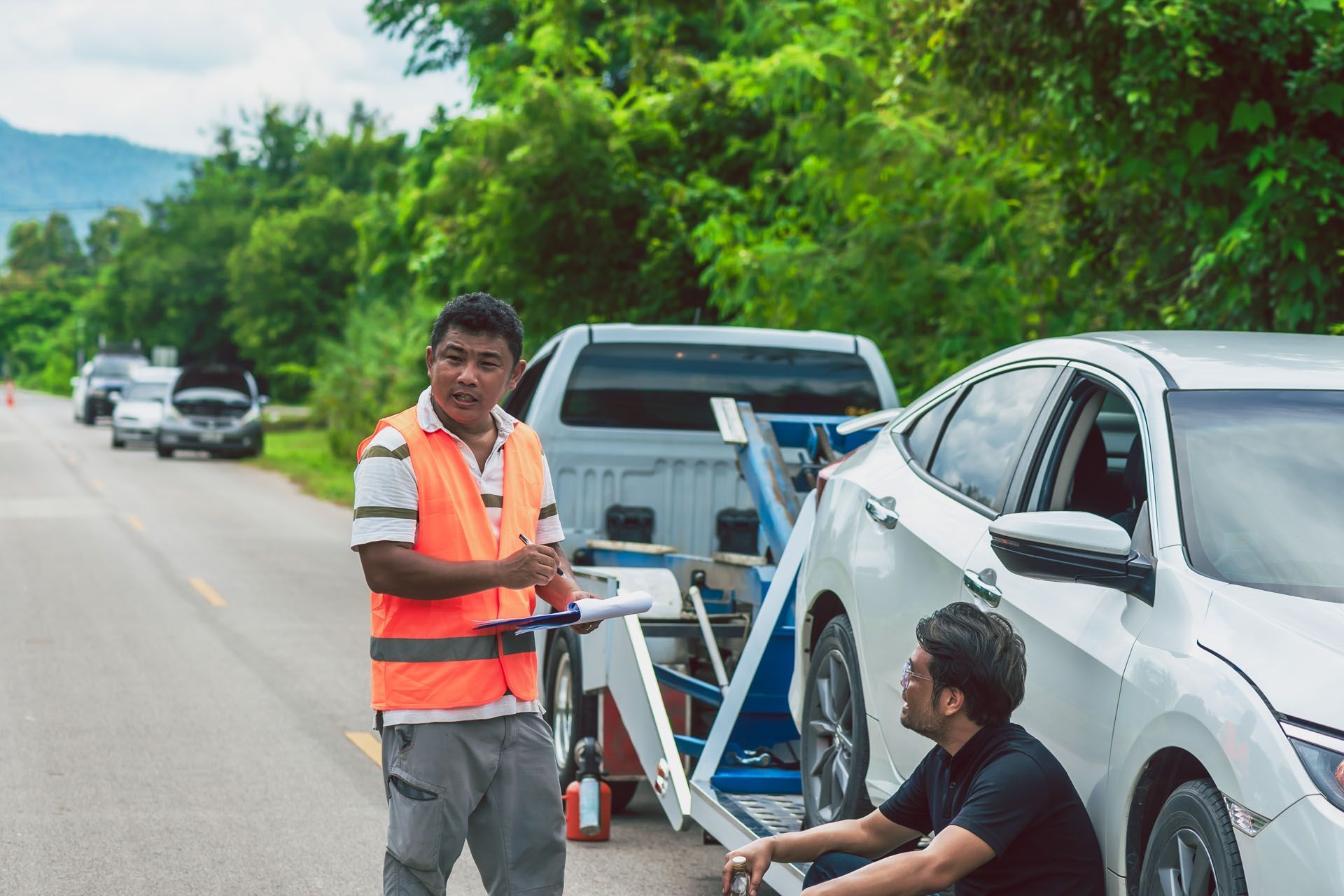 Two men are standing next to a broken down car on the side of the road.