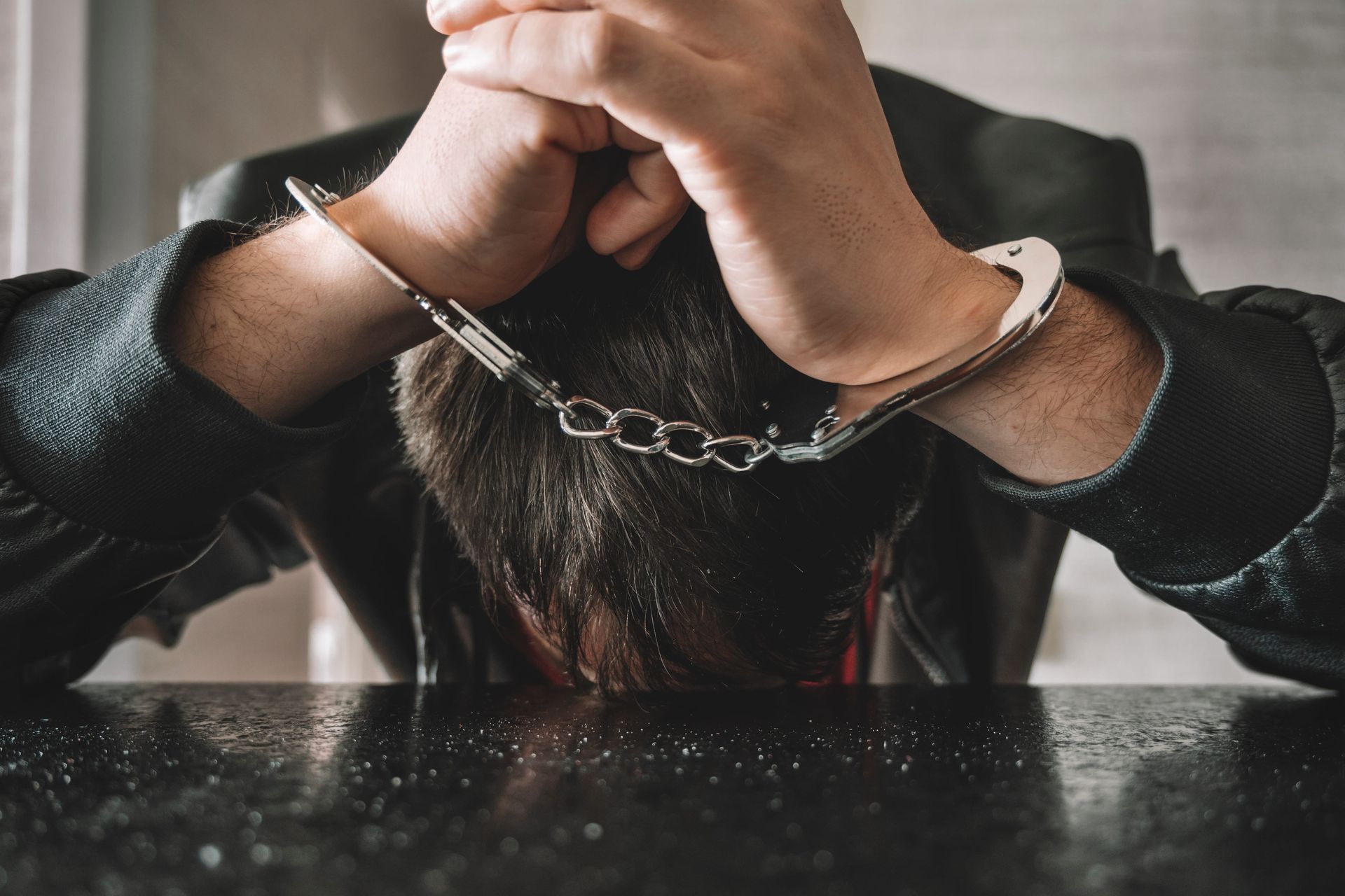 Person with chained wrists holding their head down on a table in a dark room