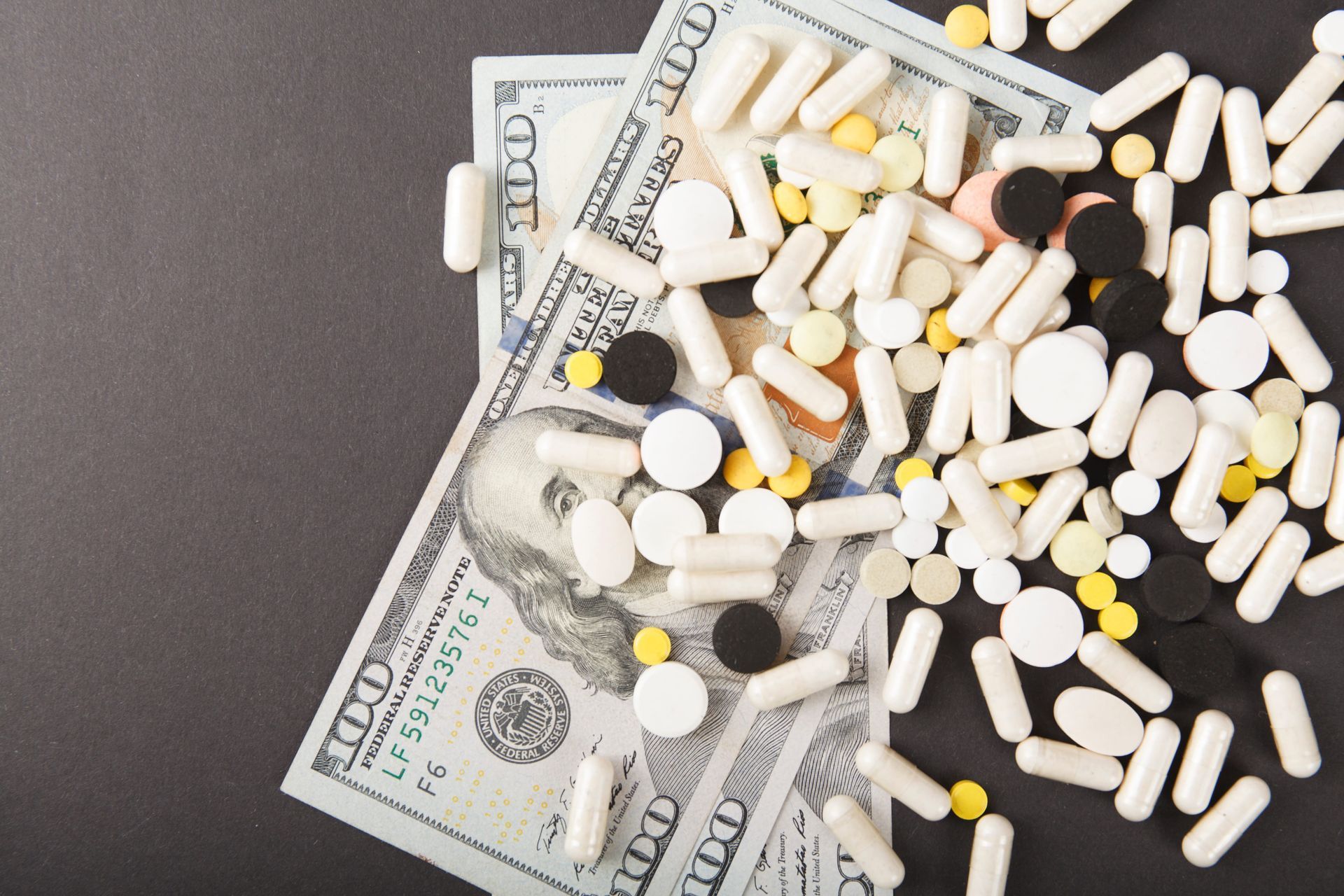 Pills scattered over U.S. dollar bills on a dark background