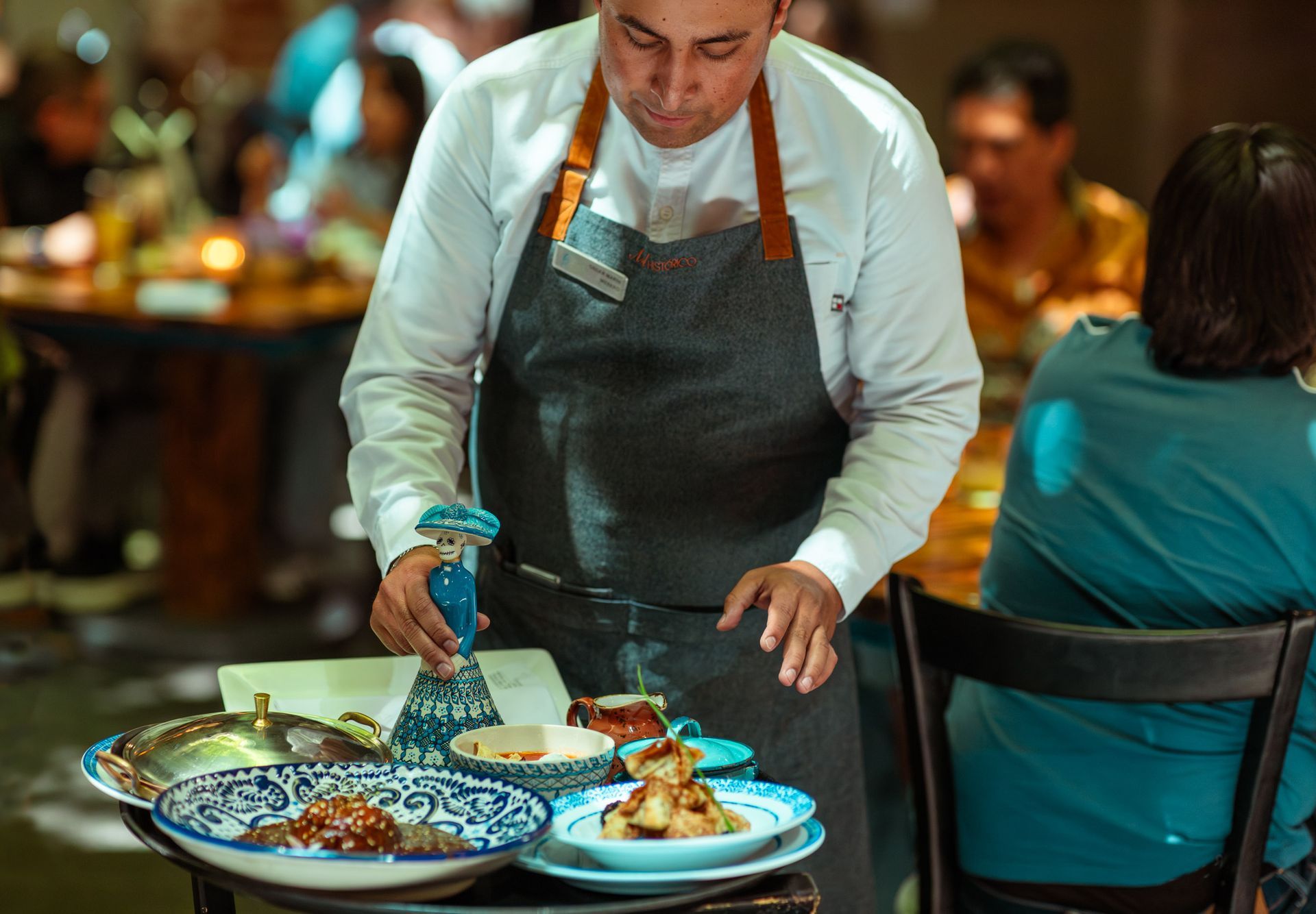 Camarero sirviendo comida en una mesa de restaurante con varios platos y cuencos.