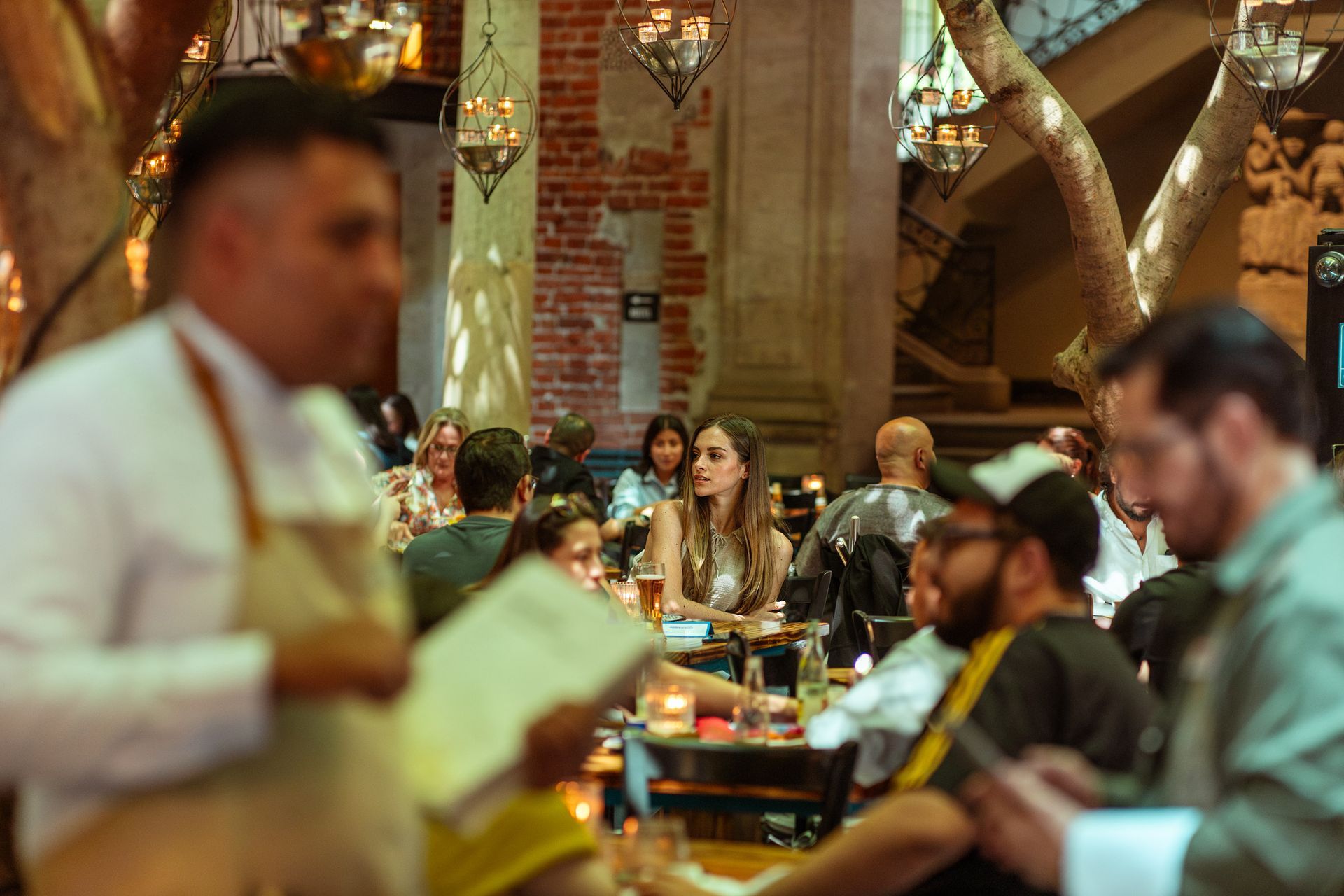 Comedor de restaurante concurrido, con clientes sentados en mesas bajo una iluminación cálida y arcos de ladrillo.