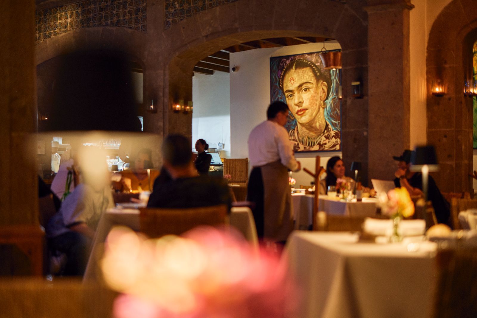 Elegante comedor de restaurante con iluminación cálida y un gran retrato en la pared del fondo.