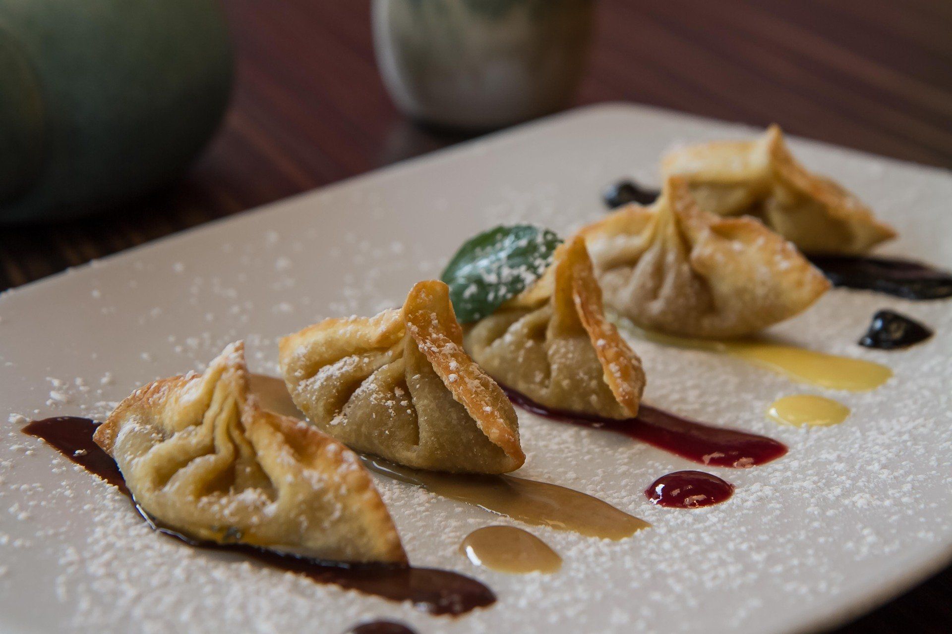 Cinco empanadillas en un plato blanco con chorritos de salsa de colores y espolvoreadas con azúcar glas.