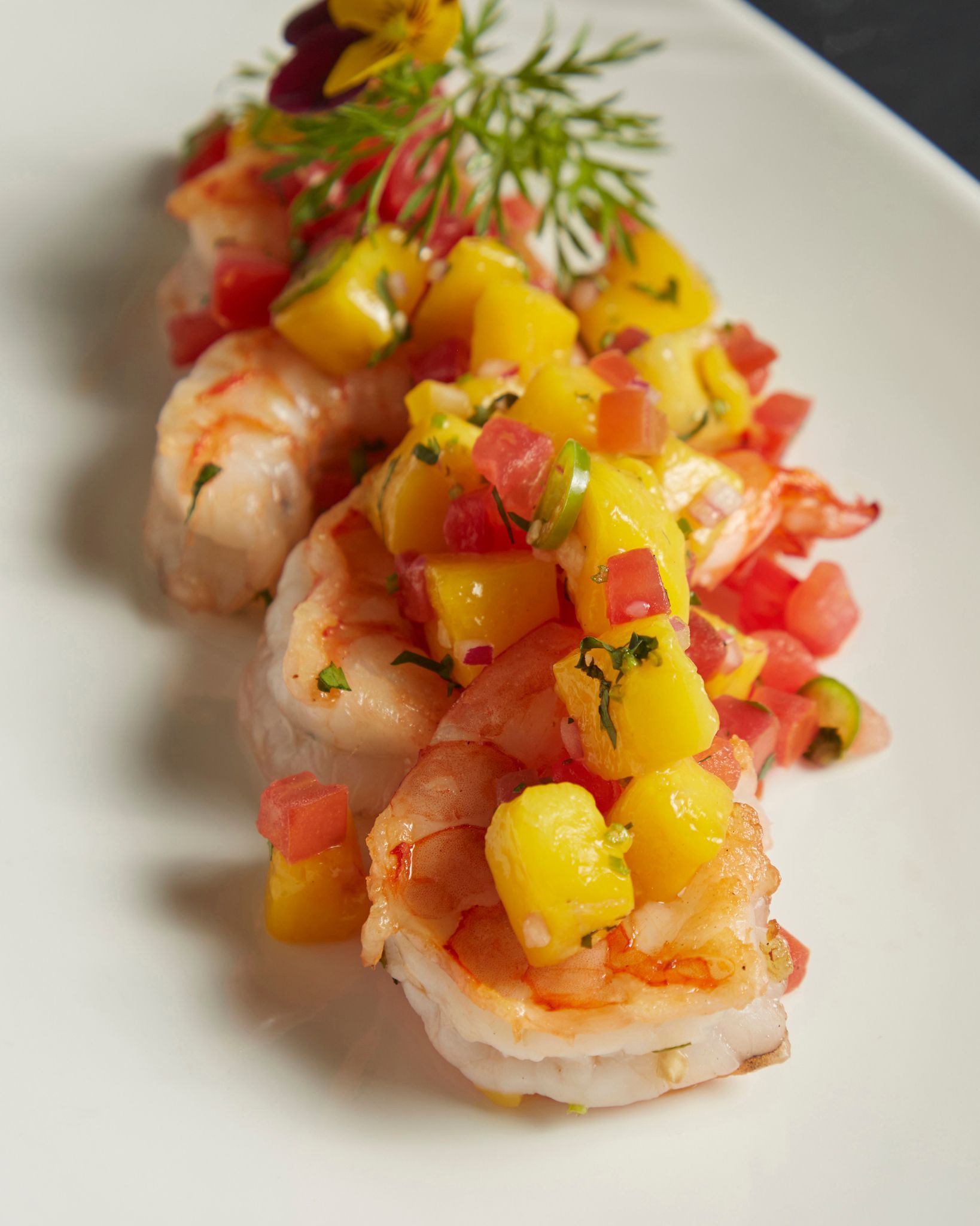 Ceviche de camarones cubierto con mango y tomate picados en un plato blanco.
