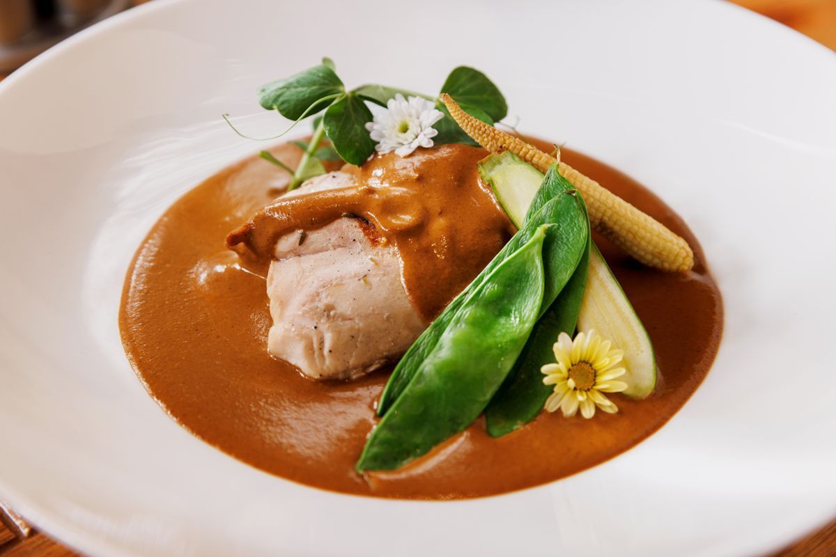 Plato gourmet presentado en un plato blanco con carne en salsa marrón, verduras verdes y flores comestibles.