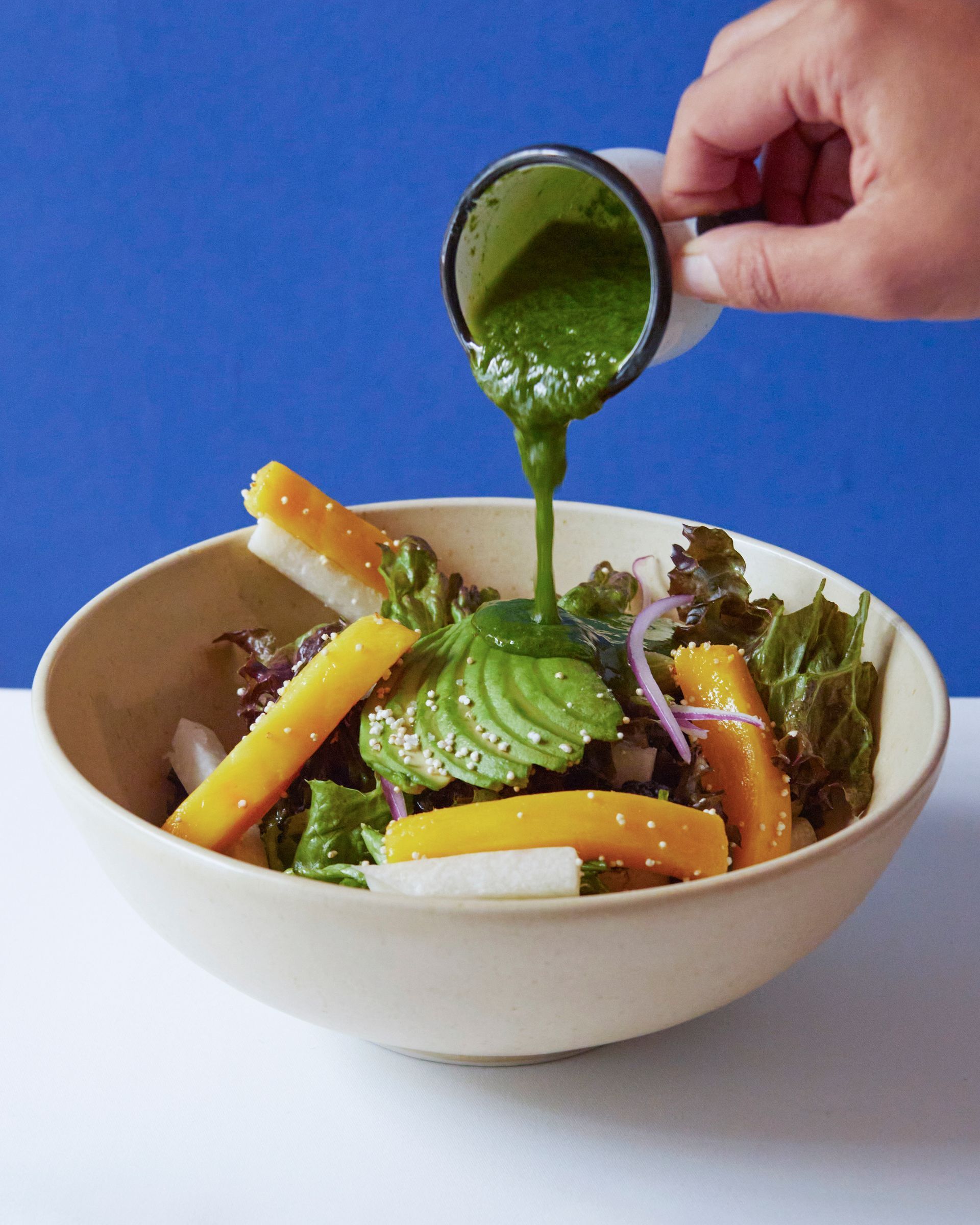 Verter a mano salsa verde sobre un tazón de ensalada con verduras coloridas.