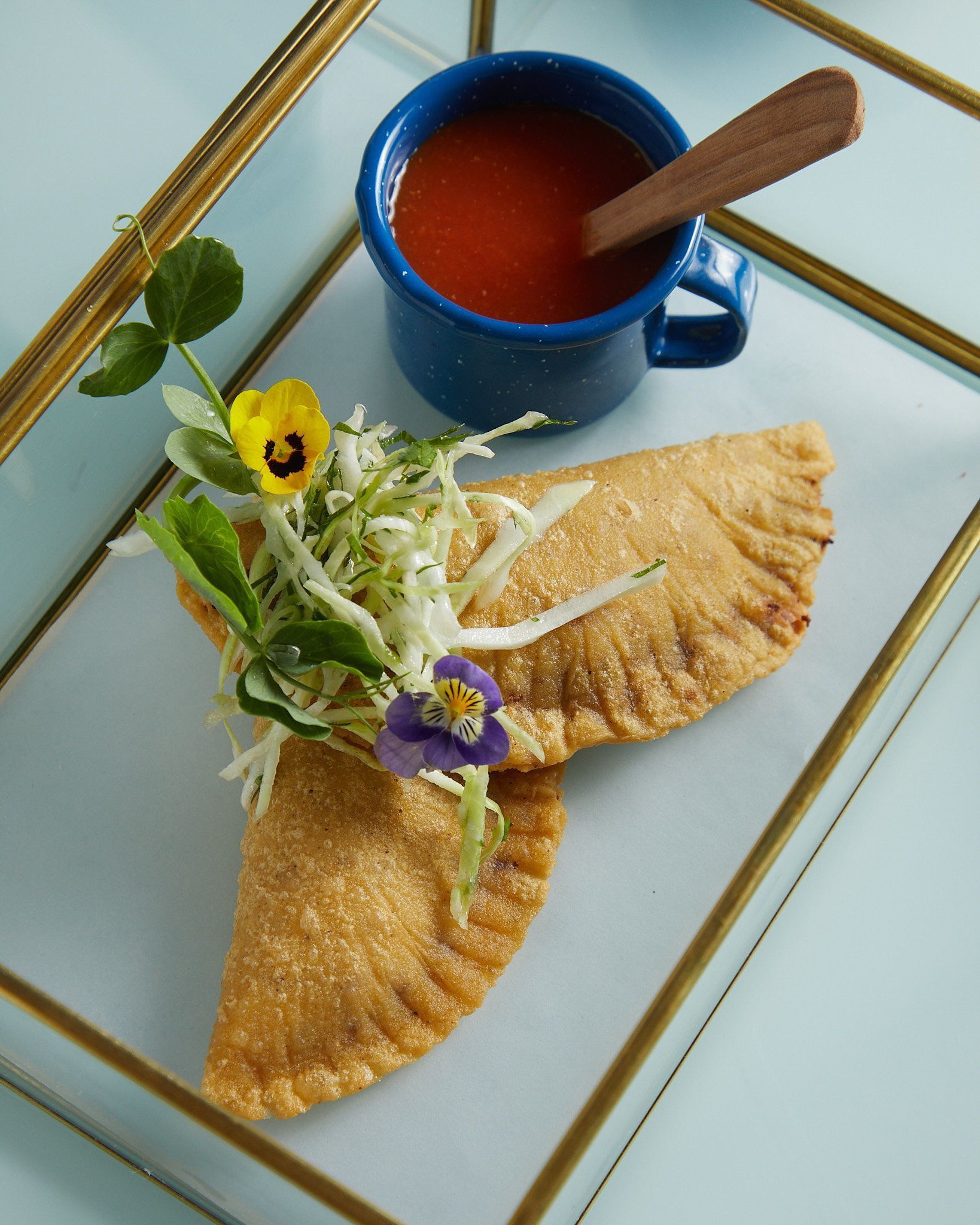 Taza azul con bebida roja, guarnición de hierbas y dos crepes dorados doblados sobre un plato blanco.