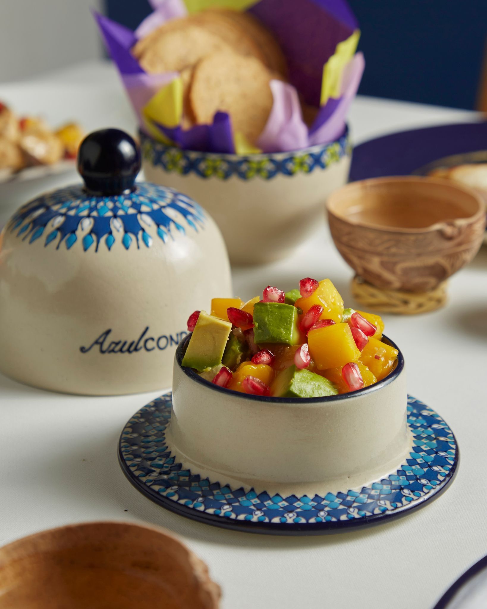 Tarta de frutas colorida sobre una mesa blanca con cuencos decorativos y pasteles al fondo.