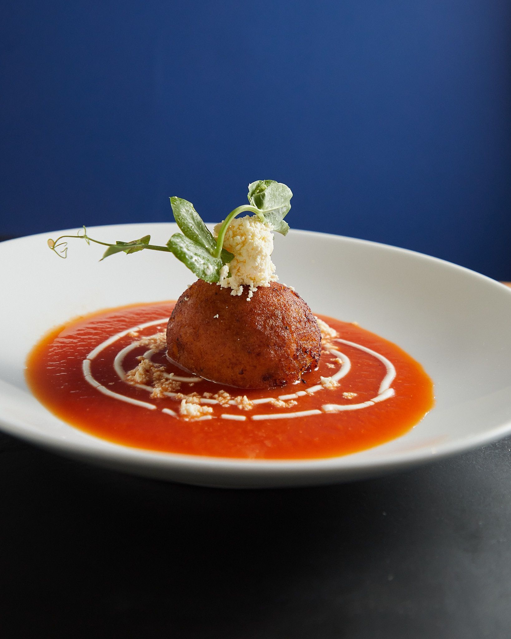Aperitivo con salsa roja, decorado con hierbas y un chorrito de crema, servido en un plato blanco.