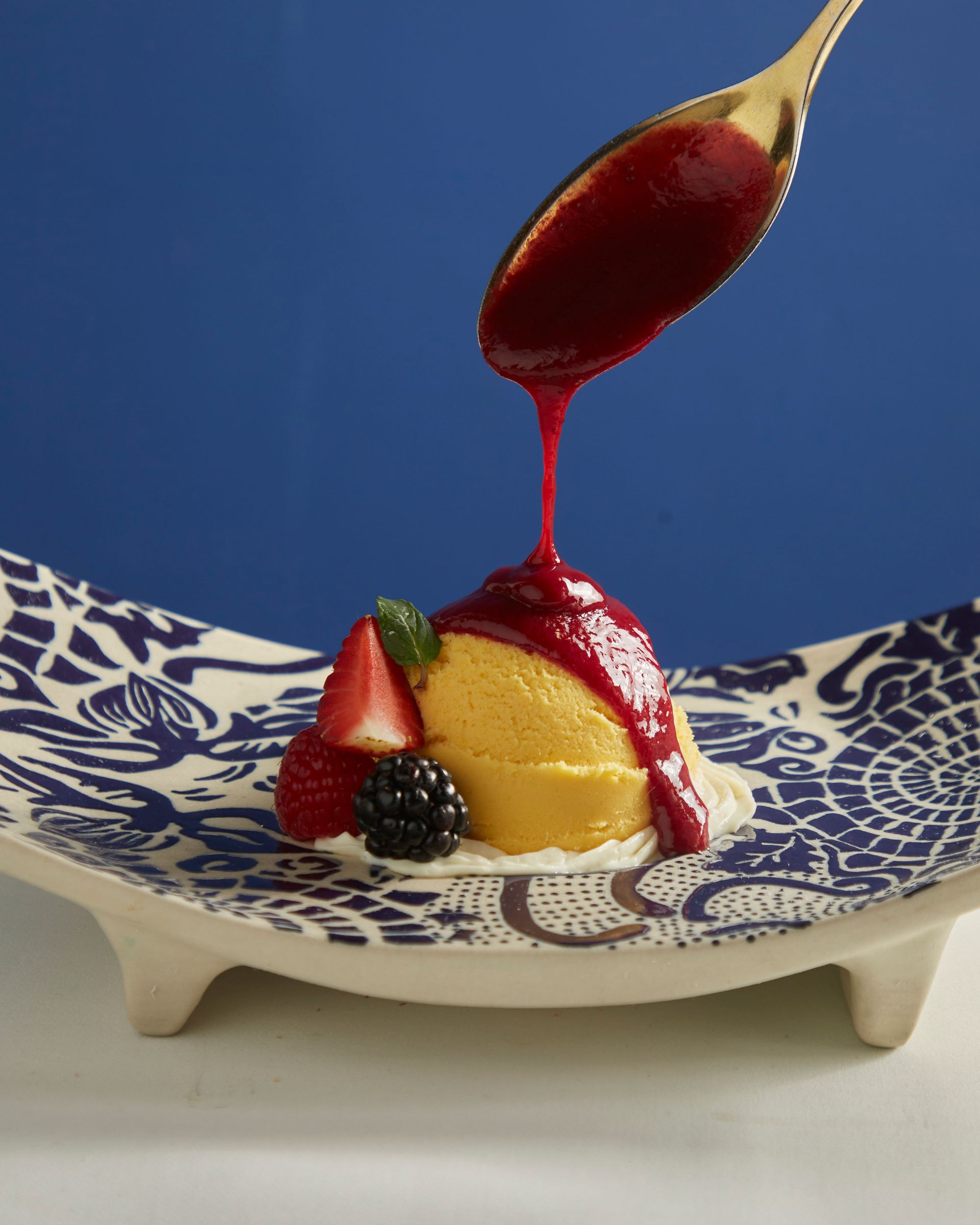 Postre en un plato azul y blanco, cubierto con salsa roja y adornado con fresas y moras.