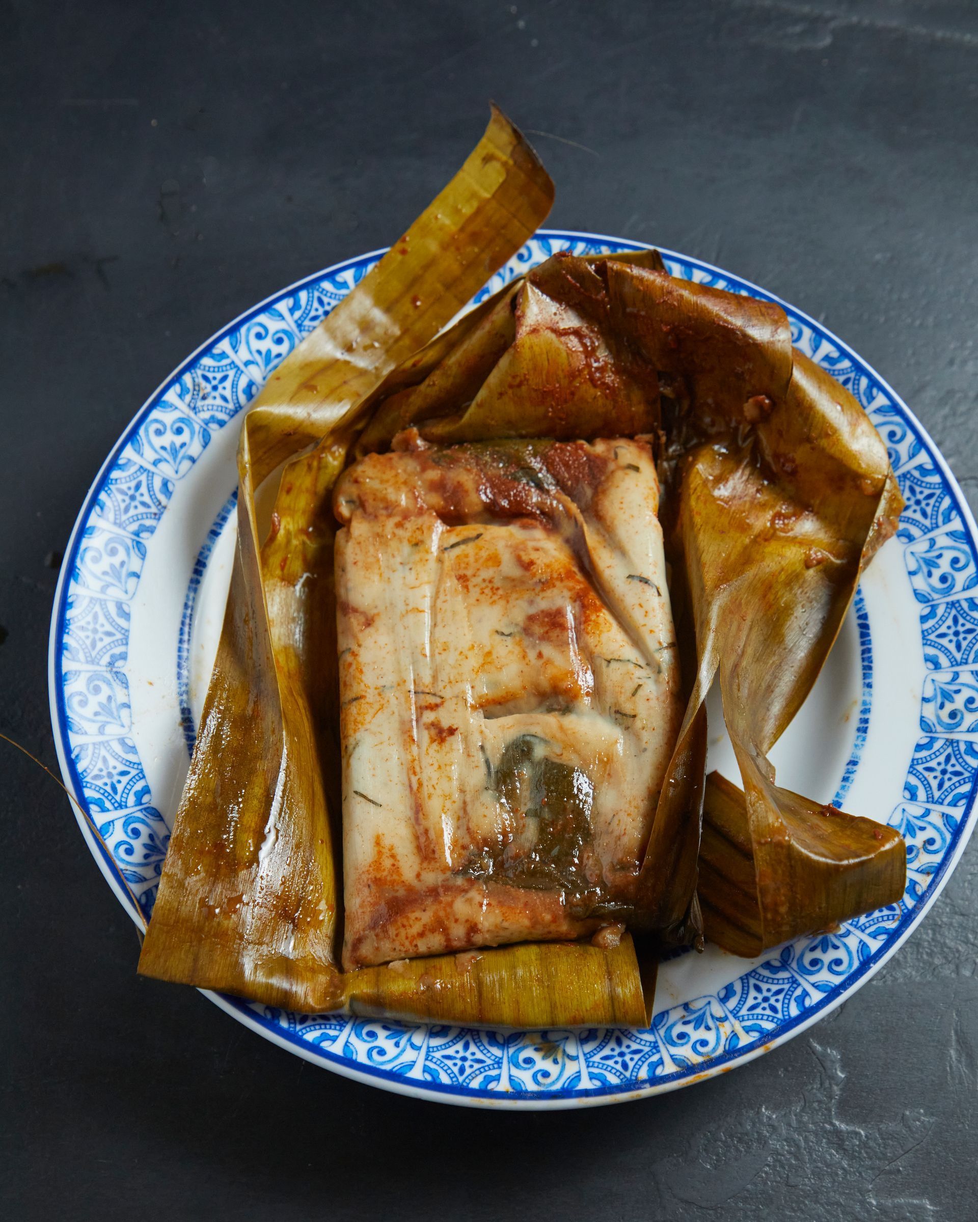 Comida abierta envuelta en hojas sobre un plato con estampado azul.