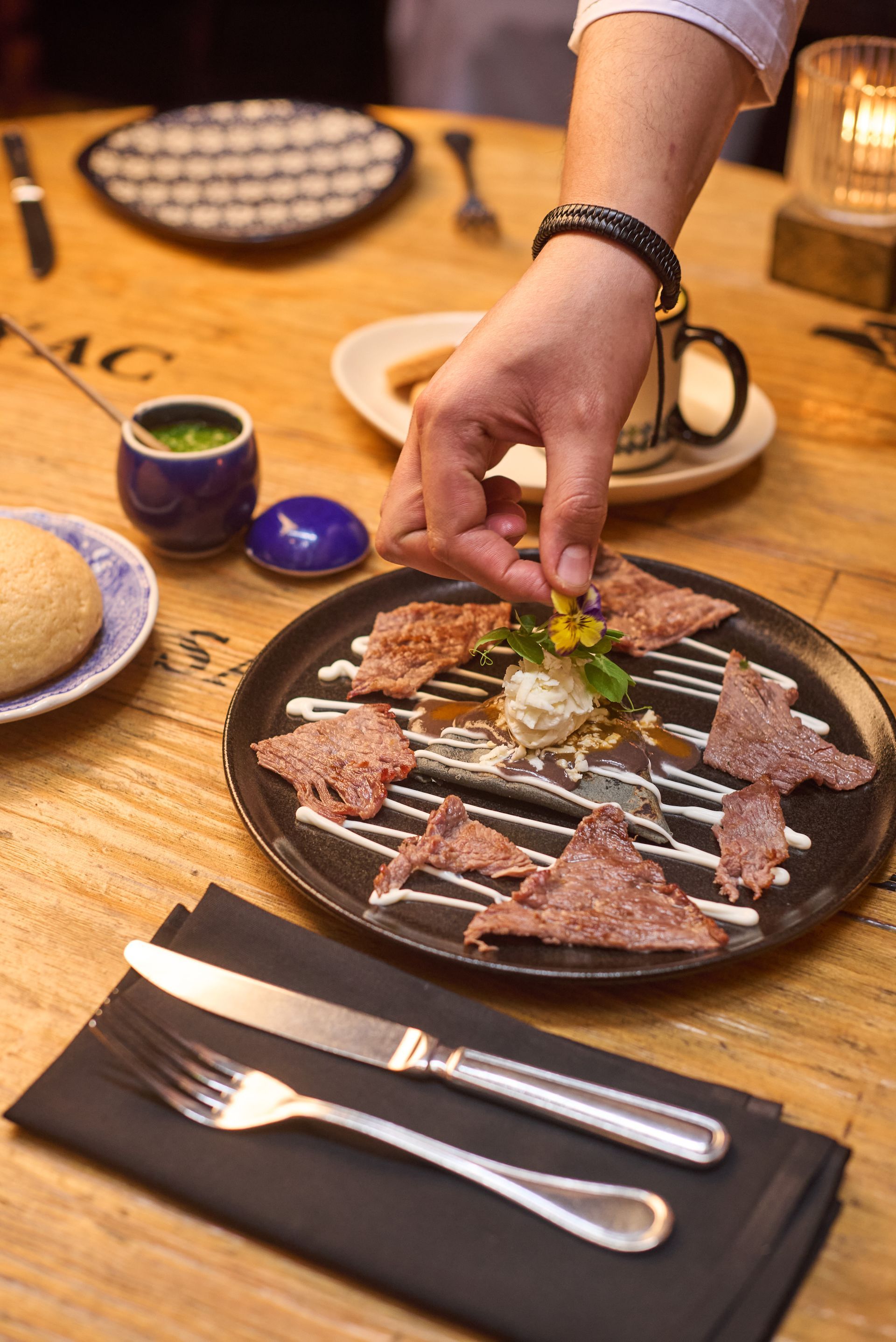 Colocando hierbas a mano sobre una fuente de carne caliente en la mesa de un restaurante.