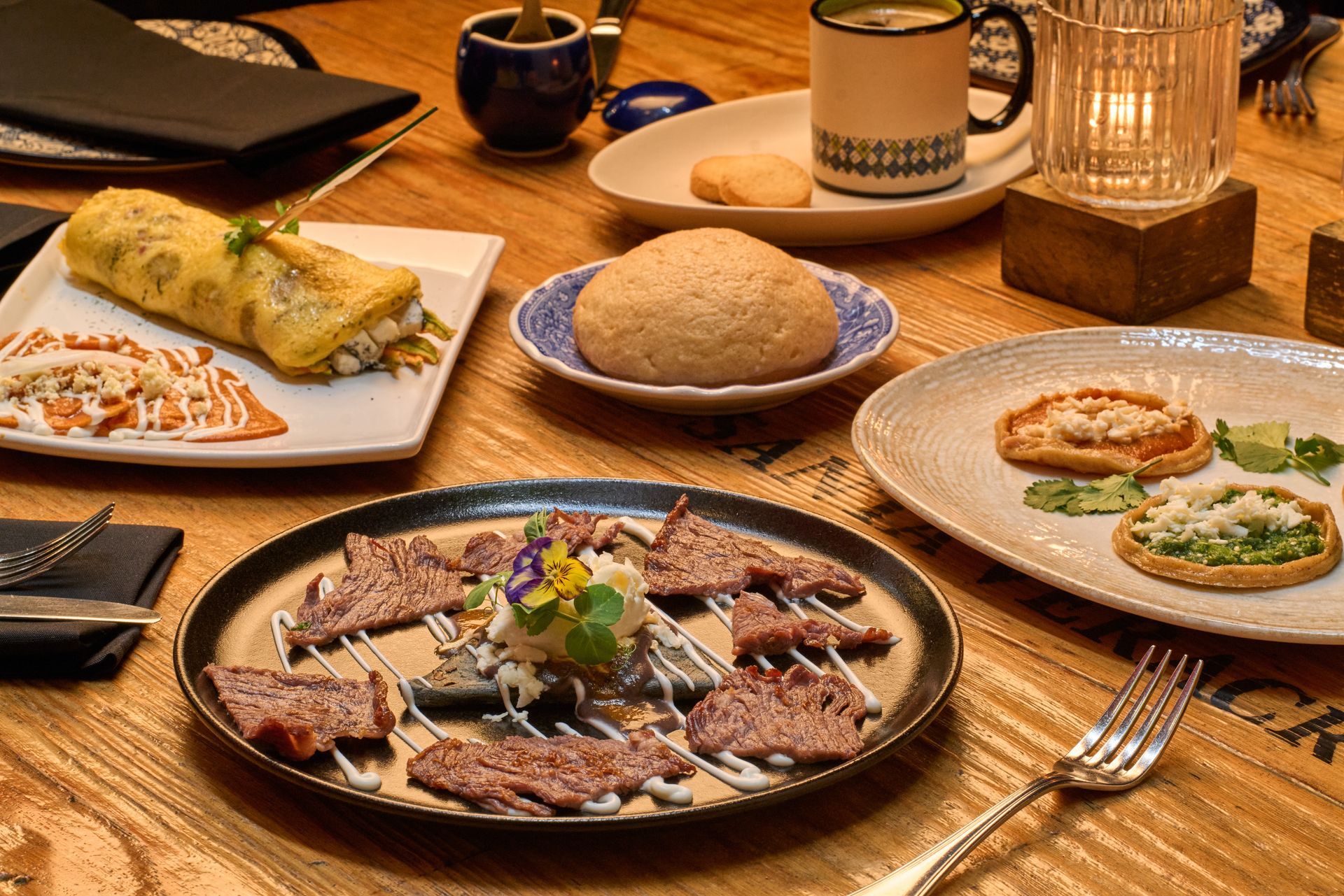 Comida mexicana servida sobre una mesa de madera con tacos, arroz, frijoles, tamales y bebidas.