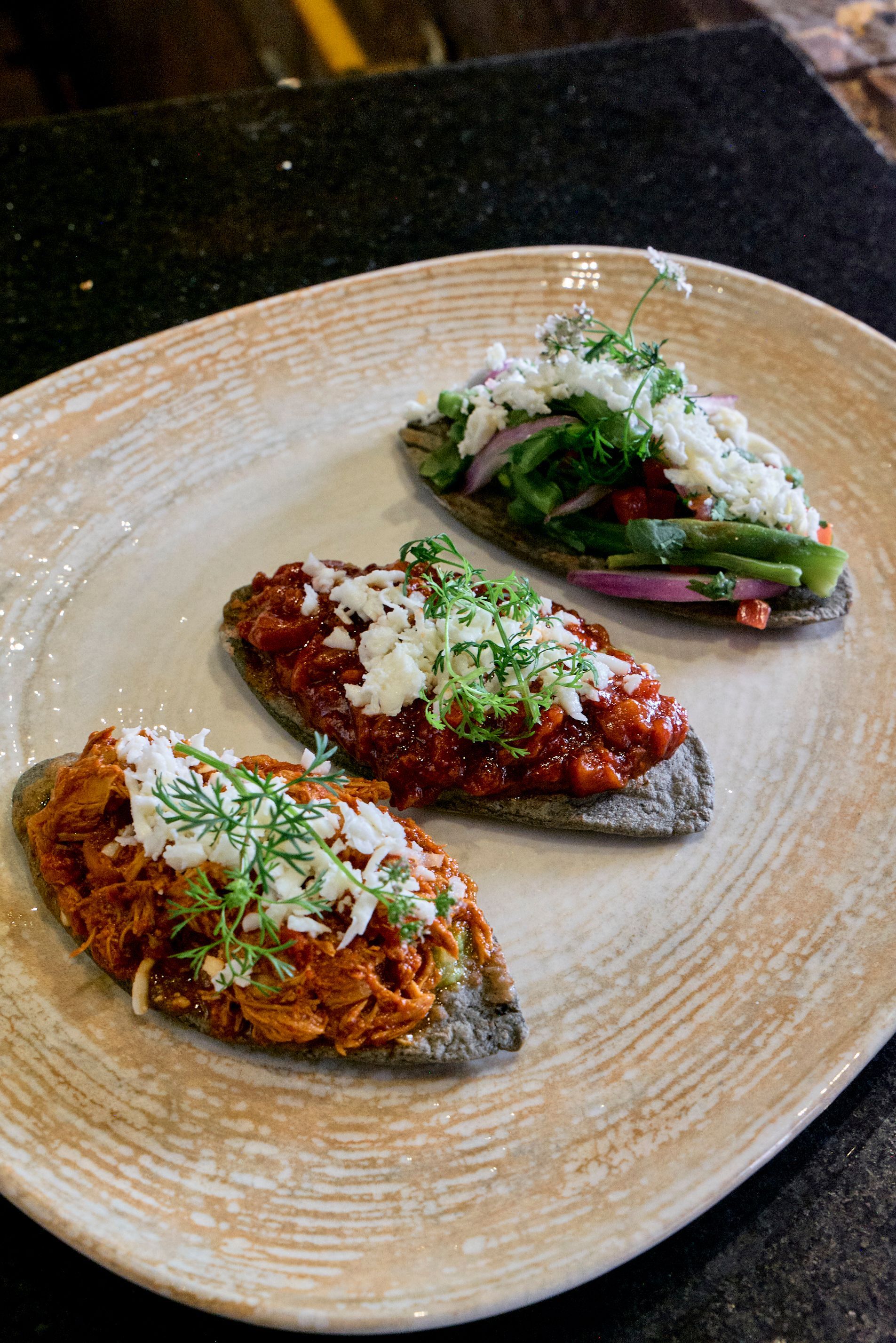 Tres gajos de patata rellenos, cubiertos con hierbas y salsa, servidos en un plato beige.