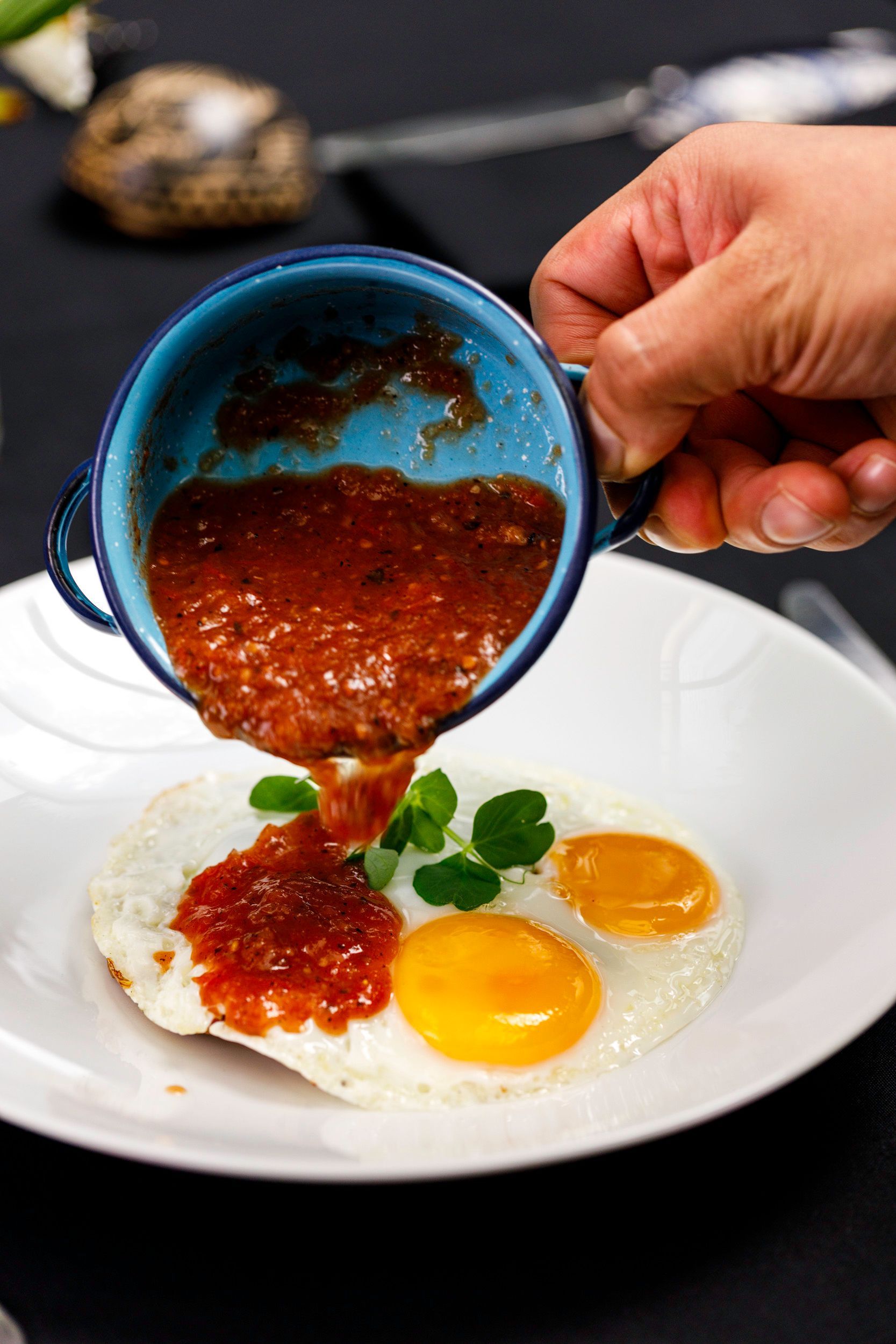 Verter a mano salsa roja de una taza azul sobre un plato de huevos y arroz.