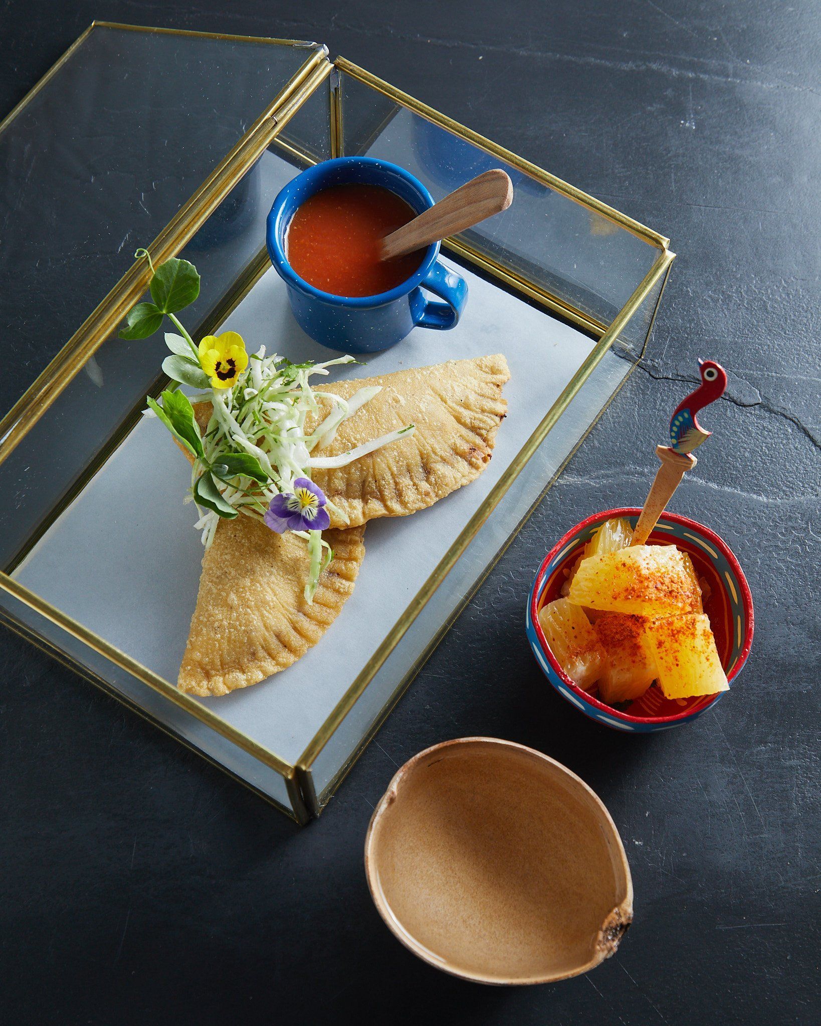 Platos de postre en una bandeja: galletas enrolladas, fruta y una taza azul con una cuchara de madera.