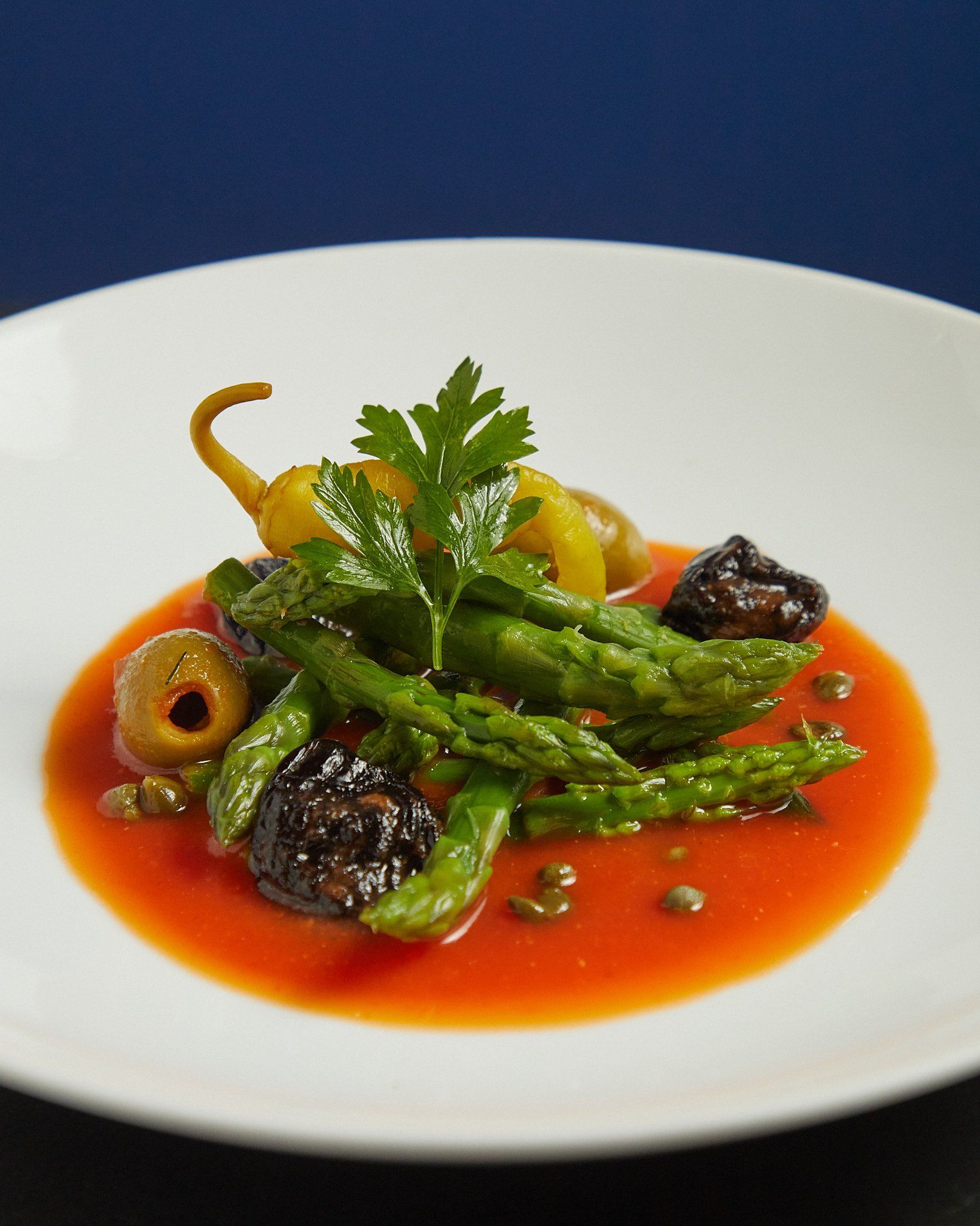 Espárragos gourmet emplatados en salsa roja, adornados con hierbas sobre un plato blanco.