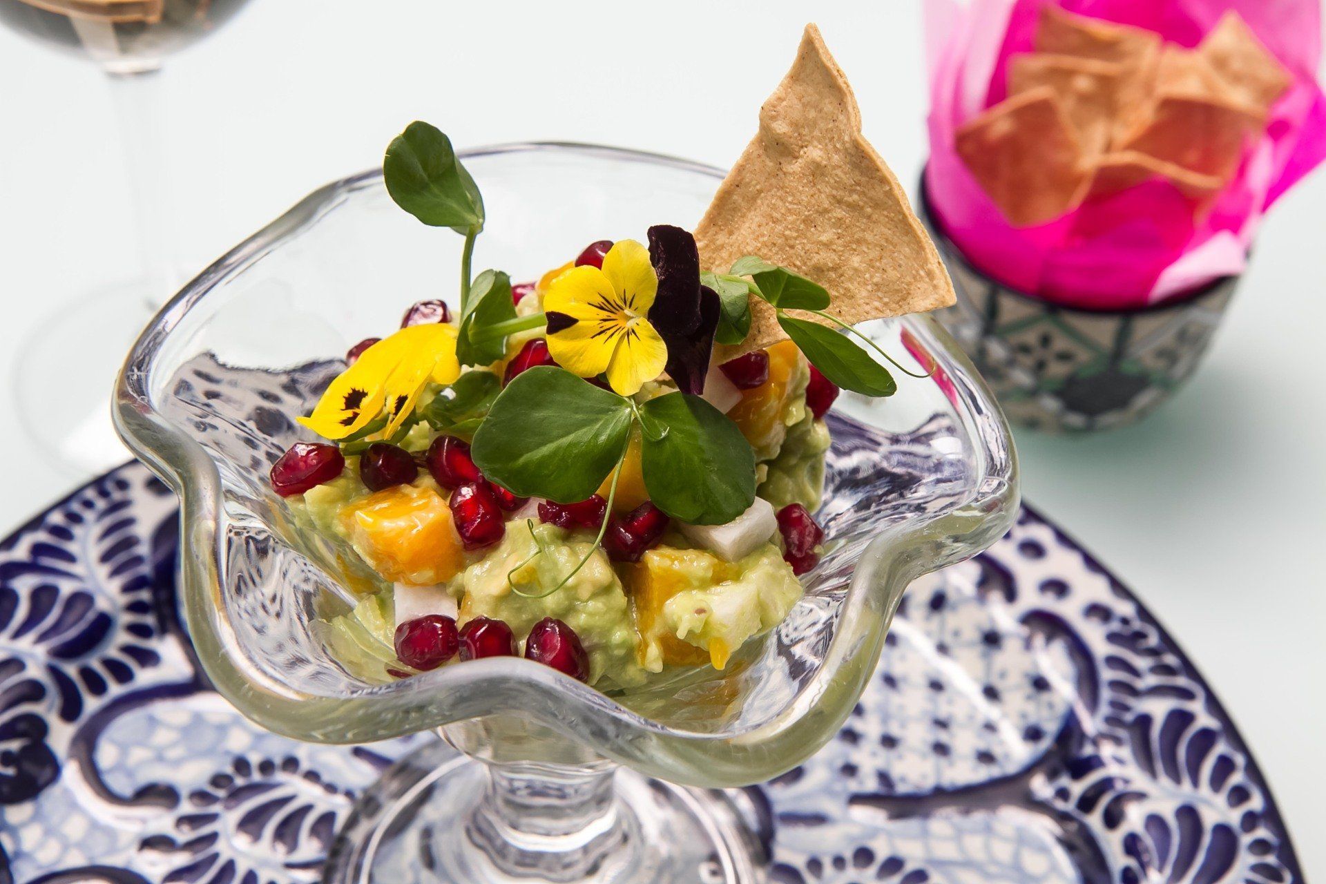 Postre en un cuenco de cristal decorado con menta y flores comestibles sobre un plato estampado.