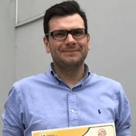 Un hombre que lleva gafas y una camisa azul sostiene un certificado.