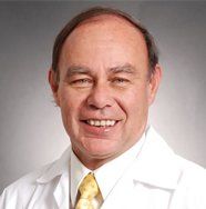 Un hombre con bata blanca y corbata sonríe a la cámara.