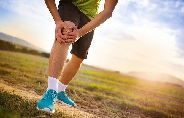 Una persona se sostiene la rodilla con dolor mientras corre en un campo.