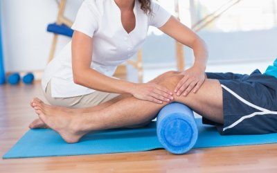 Una mujer está masajeando la pierna de un hombre con un rodillo de espuma azul.