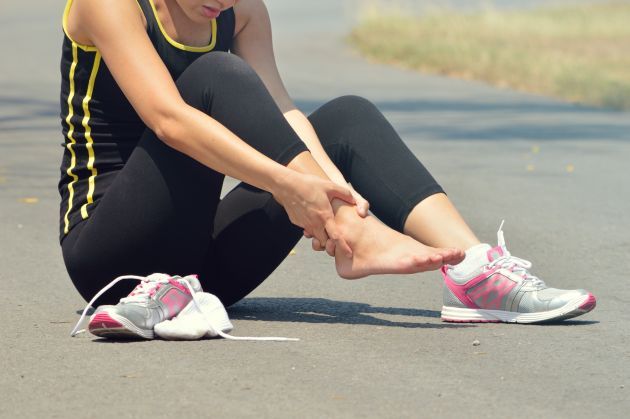 Una mujer está sentada en el suelo sujetándose el tobillo.