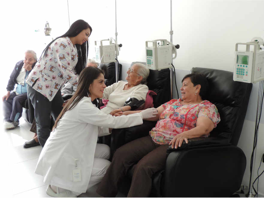 Una especialista y su asistente administrando tratamientos especializados a varios pacientes en una sala de administración de medicamentos