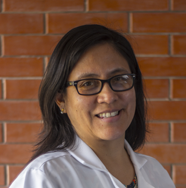Una mujer que lleva gafas y una bata blanca sonríe delante de una pared de ladrillos.