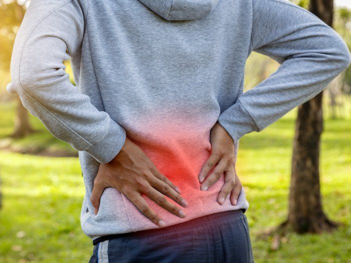 Un hombre se sostiene la espalda con dolor en un parque.