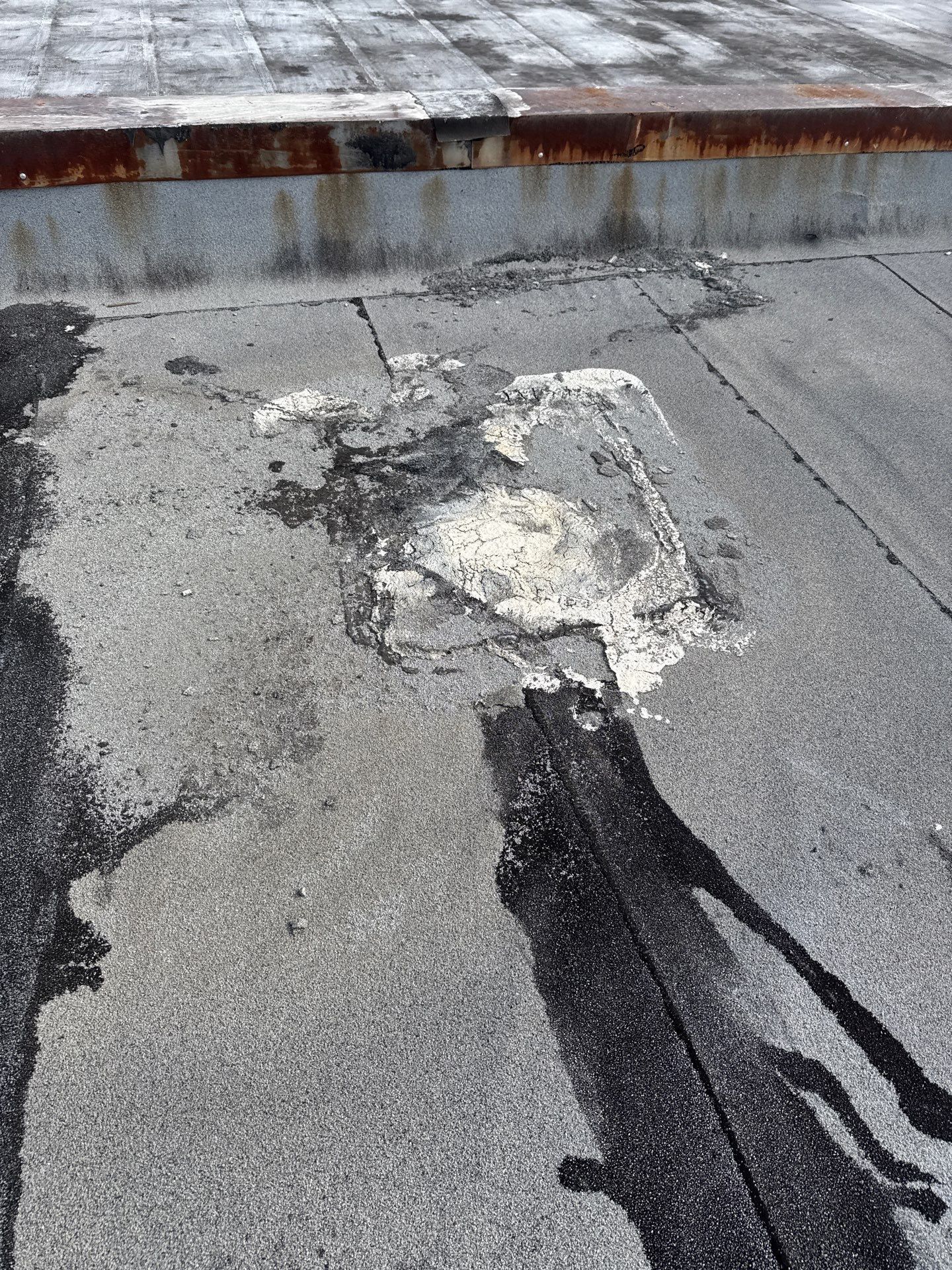 Damaged rooftop asphalt with a large patched crack and peeling sections near a low wall.