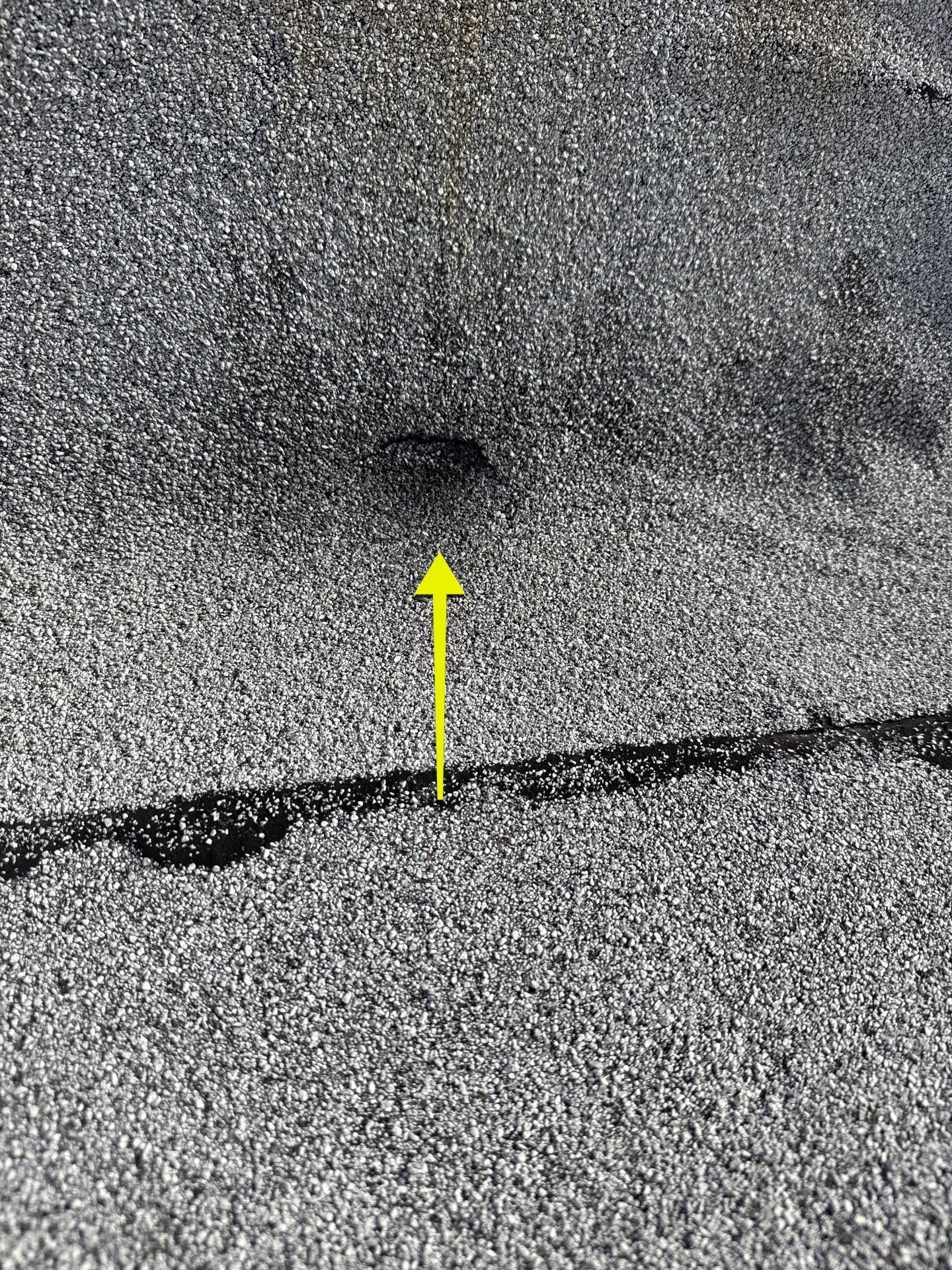 Cracked gray pavement with a yellow arrow pointing to a small dark spot.