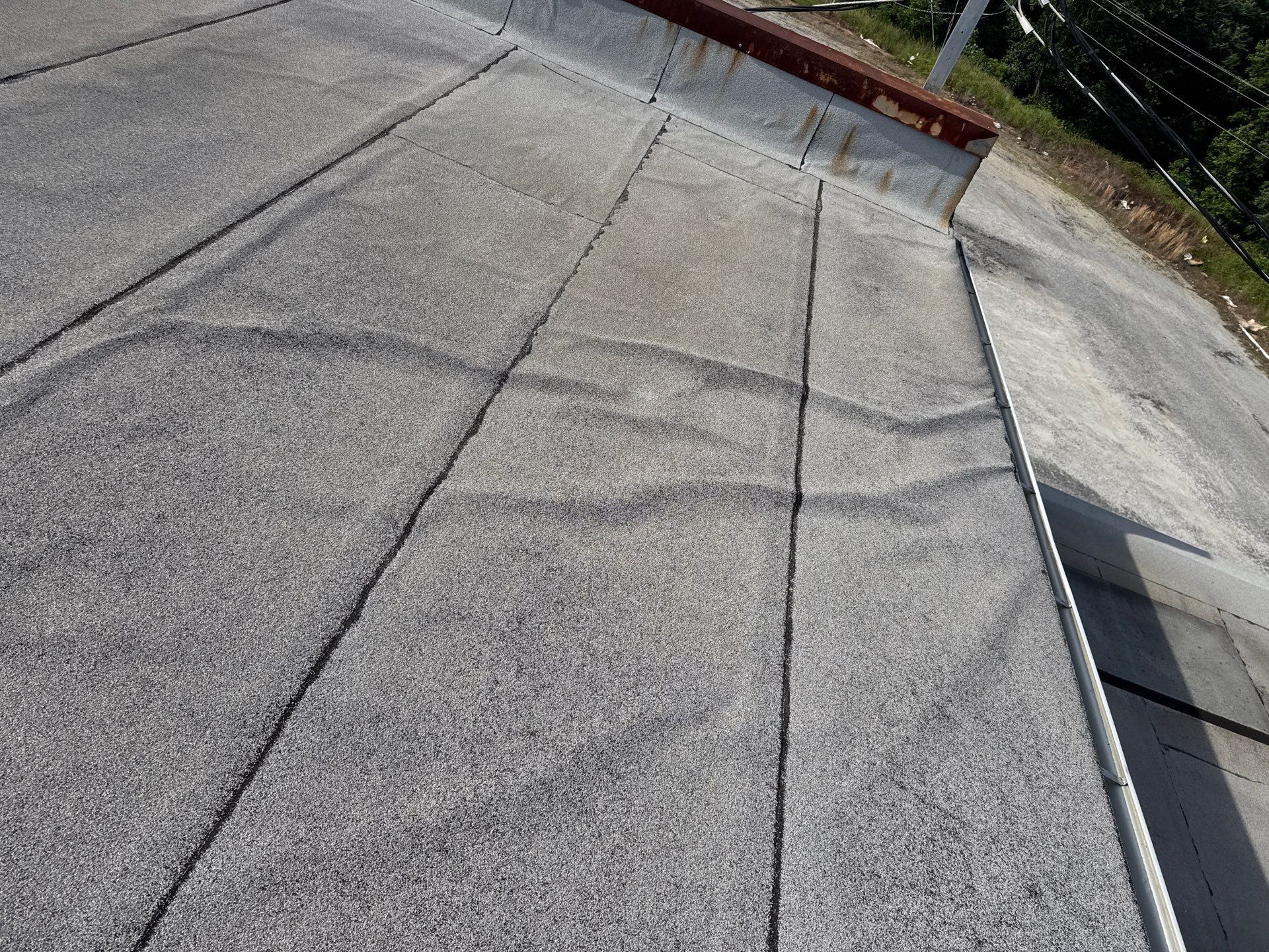 Rooftop with gray shingles and a flat gravel surface, viewed at an angle.