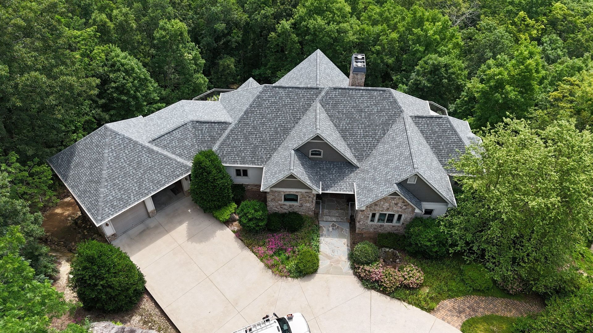 Aerial view of a gray-roofed house surrounded by dense green trees and a driveway.