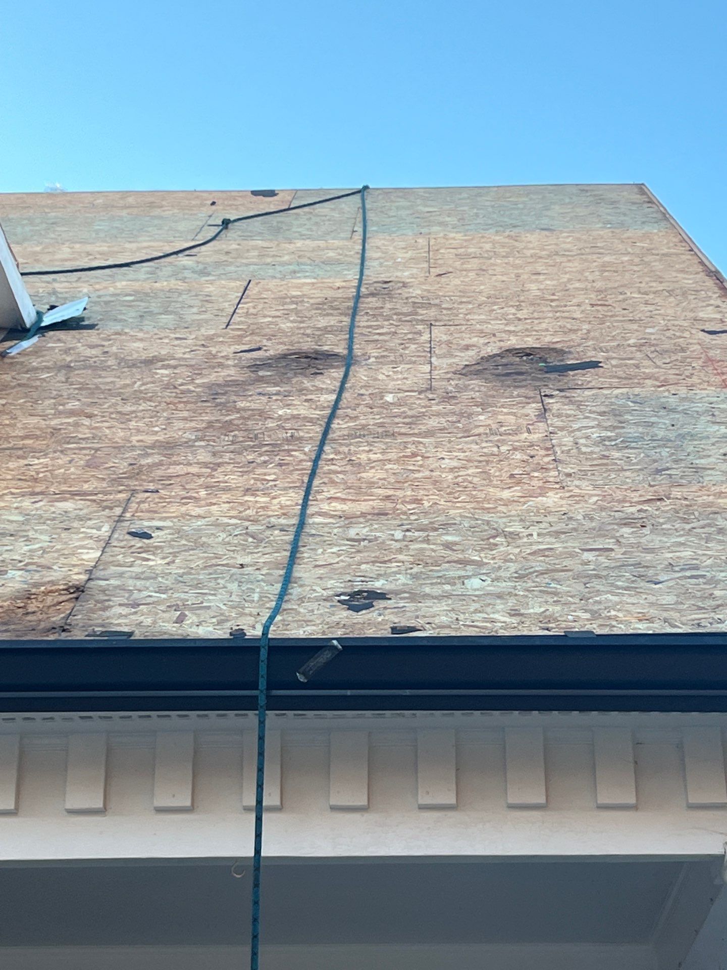 Partially roofed house with exposed plywood, a black cable, and blue sky overhead