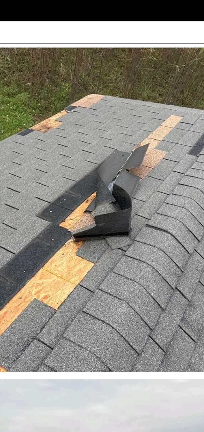 Damaged gray roof shingles with a torn black patch over a yellow roof line.