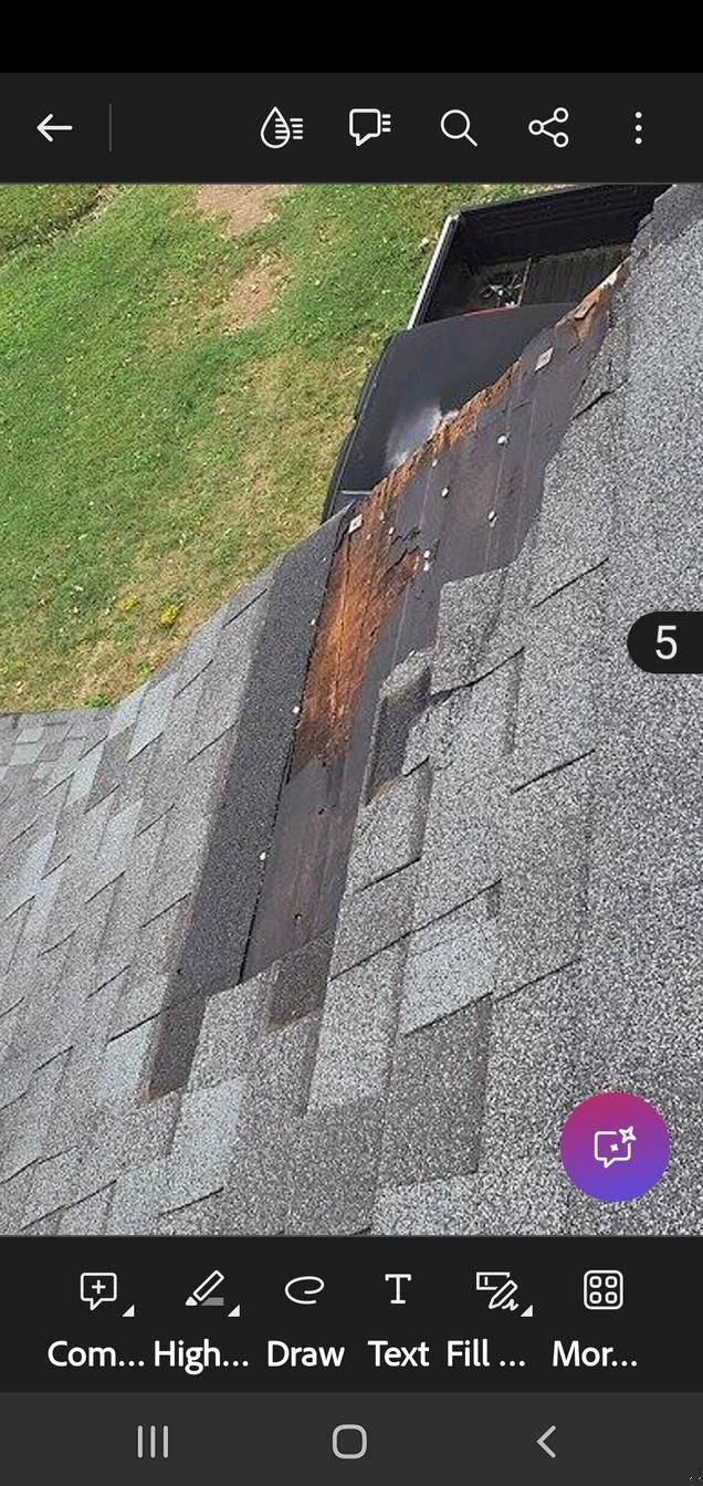 Damaged asphalt roof with a rusted metal flashing strip beside green grass and gray shingles