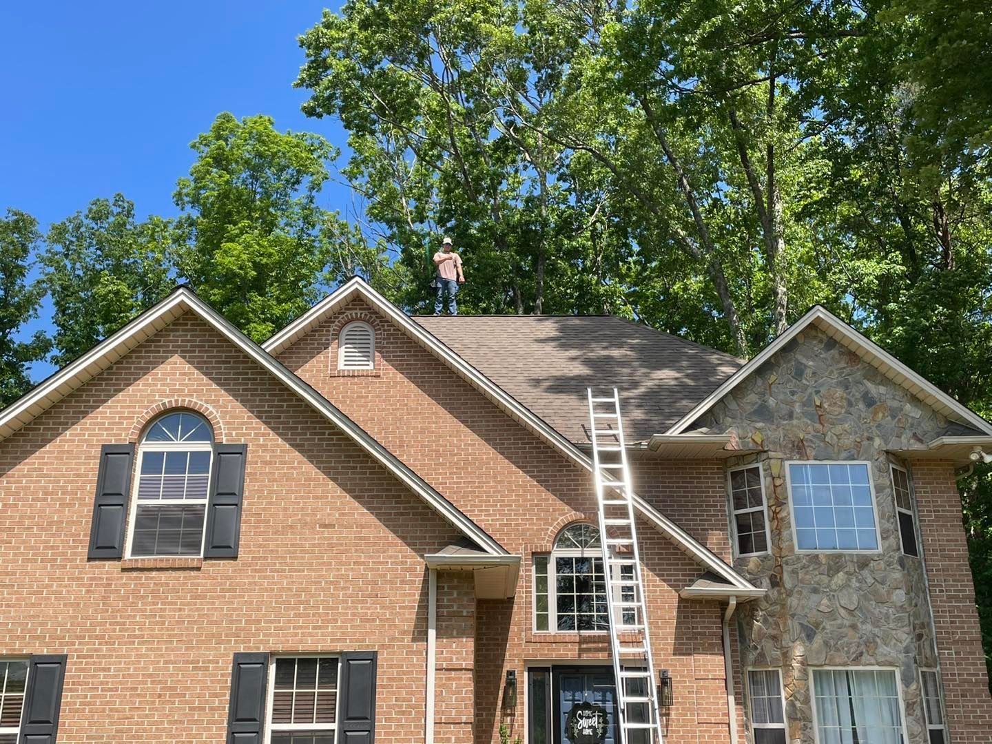 A man is standing on the roof of a large brick house.