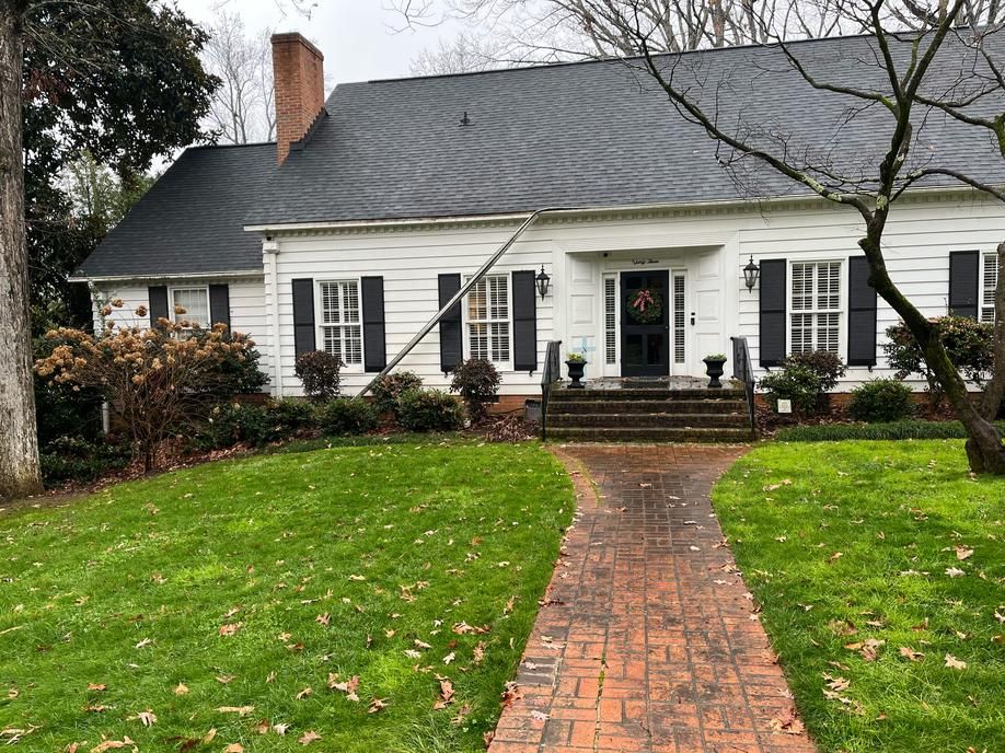 White house with black shutters and brick walkway, framed by green lawn and bare trees.