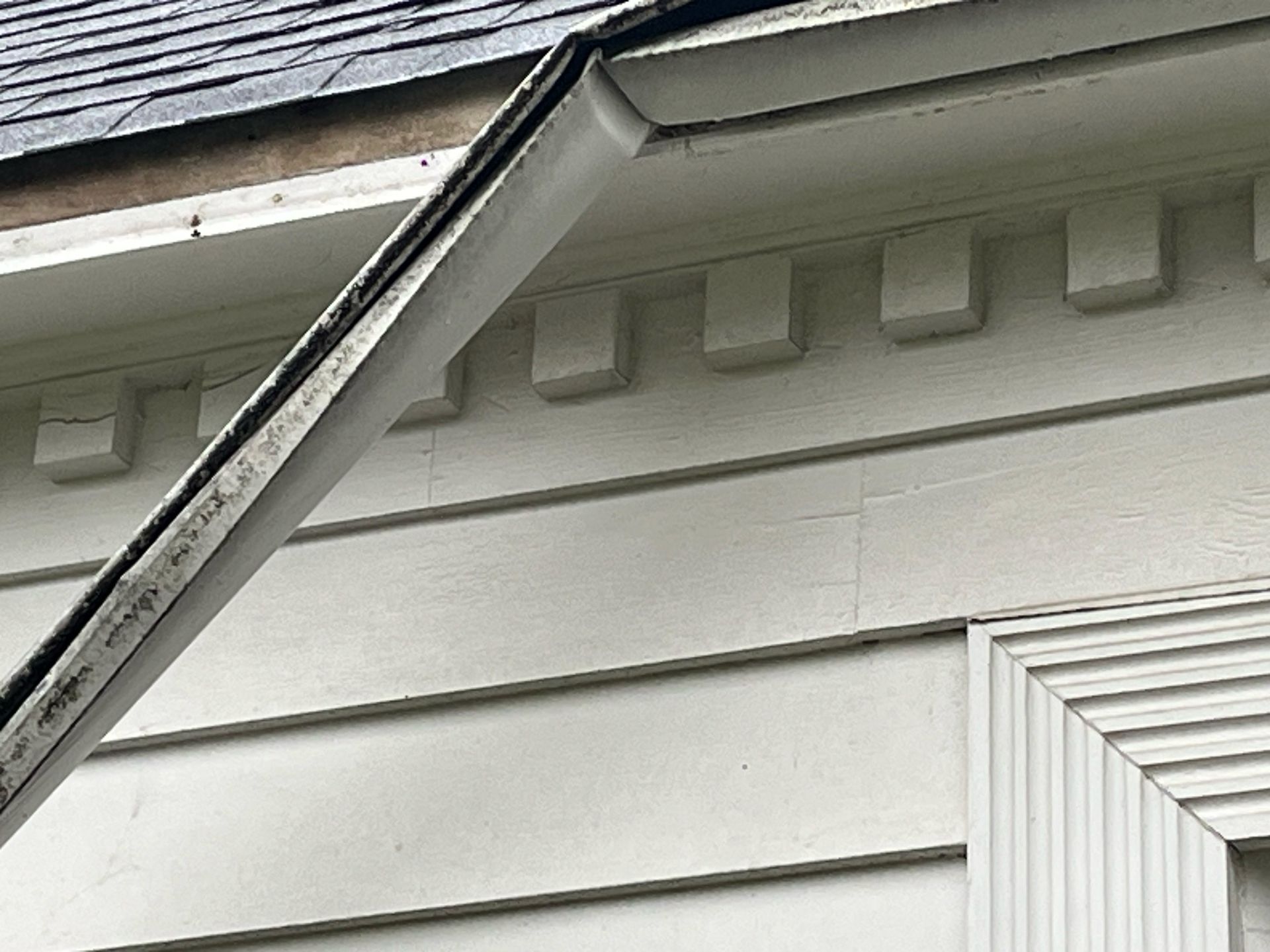 Close-up of a house roof edge with white siding and a black gutter against the eaves