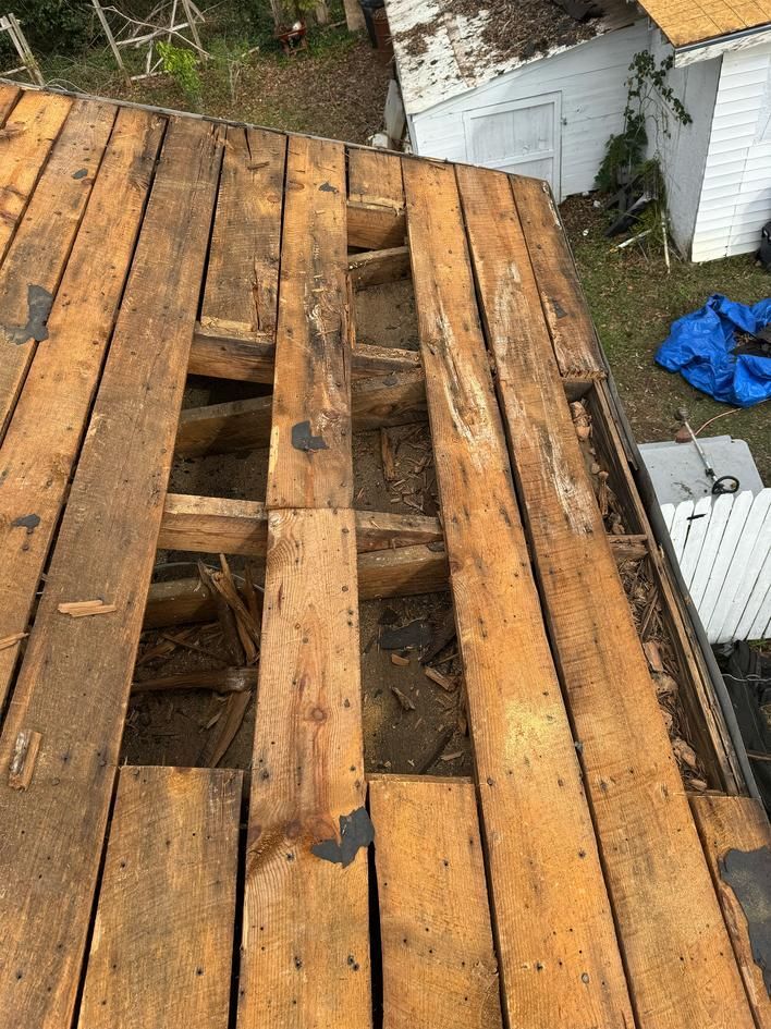 Partially dismantled wooden roof deck with missing planks and a damaged section near a yard shed