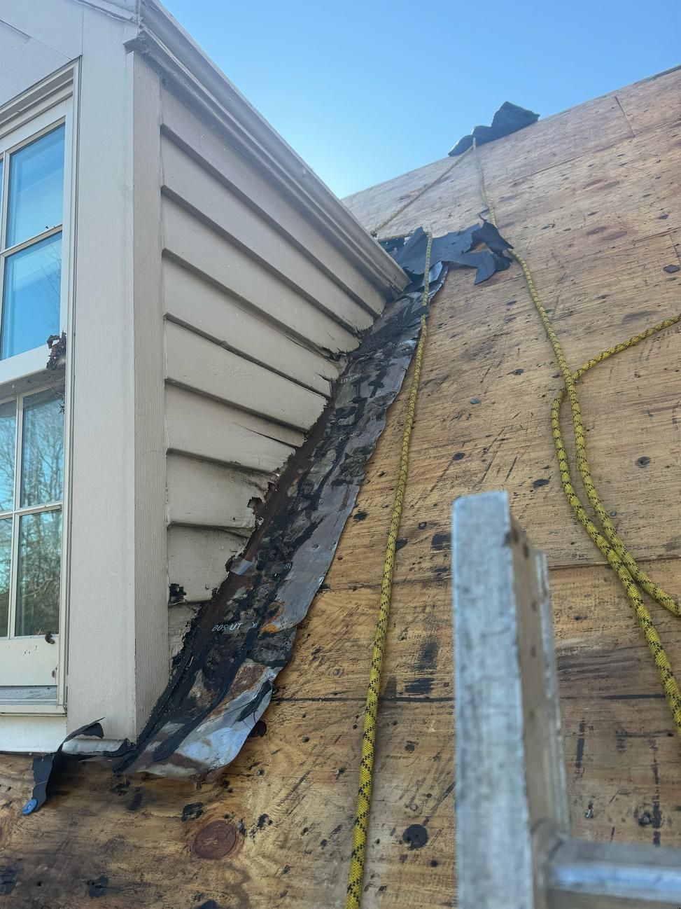 Damaged rooftop seam between two brick buildings with exposed flashing and debris.