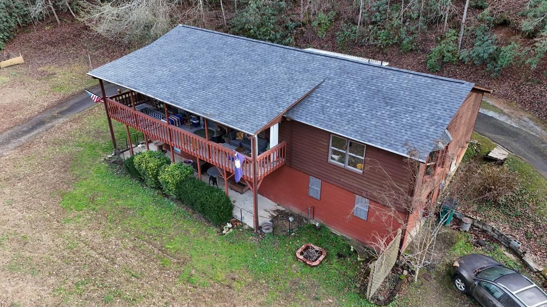 Aerial view of a brick house with a gray roof, front porch, and surrounding yard