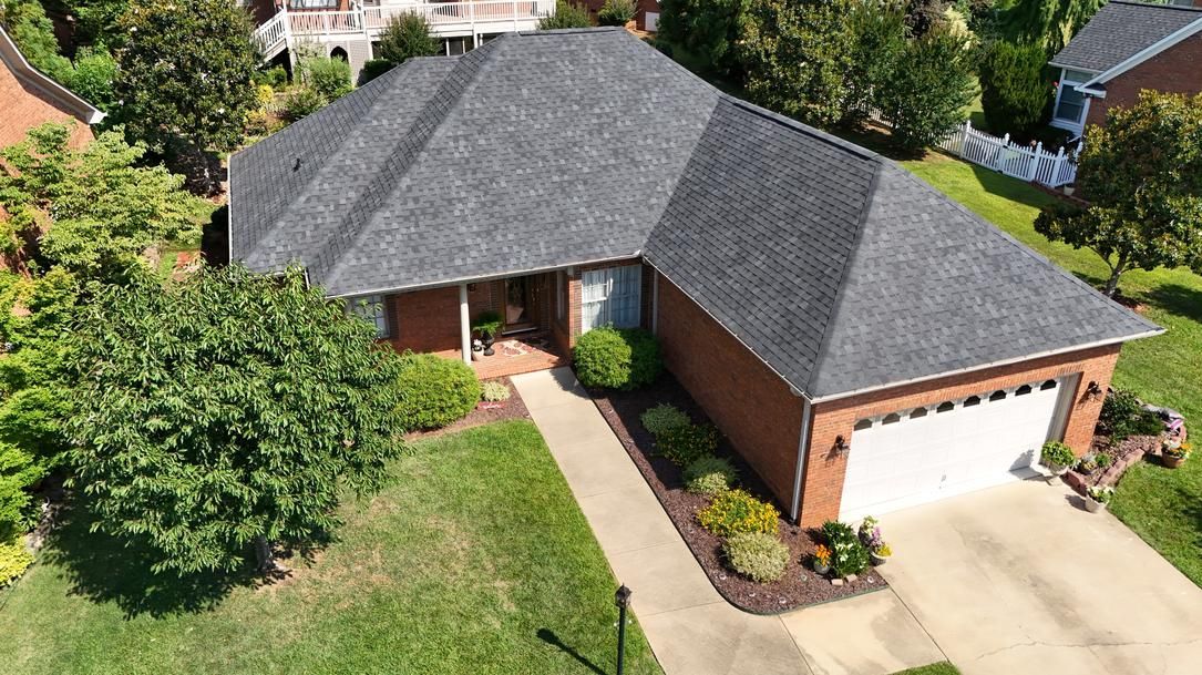 Aerial view of a brick suburban house with a gray roof, front lawn, driveway, and two-car garage.