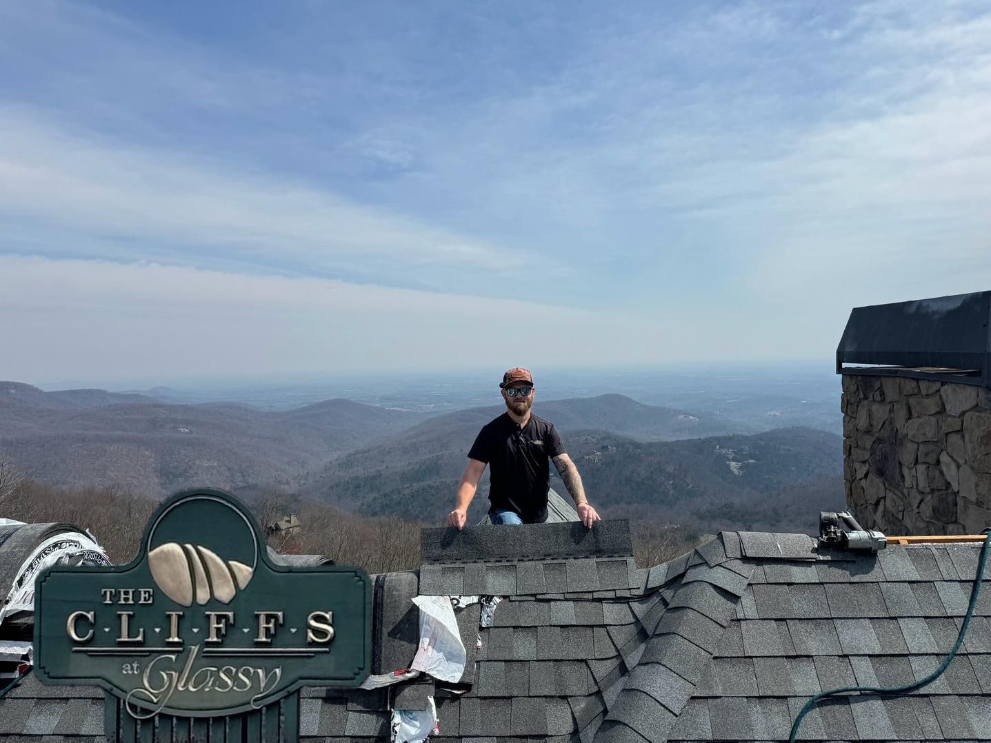Person on a rooftop lookout with “The Cliffs” sign, overlooking hazy mountains under a blue sky