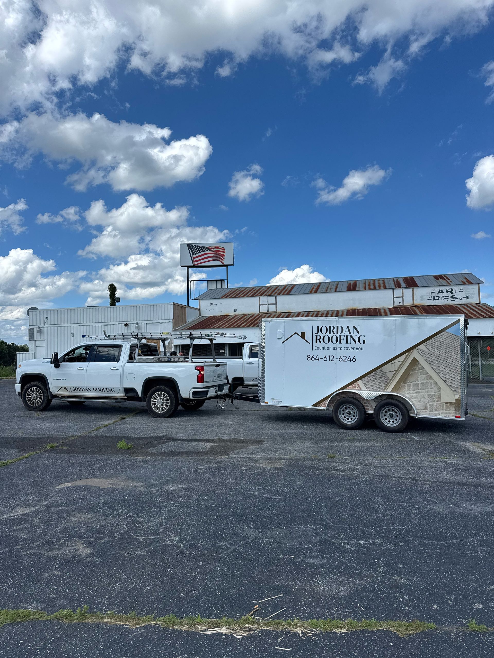 White pickup towing a white enclosed trailer on a gravel lot under a blue sky with clouds