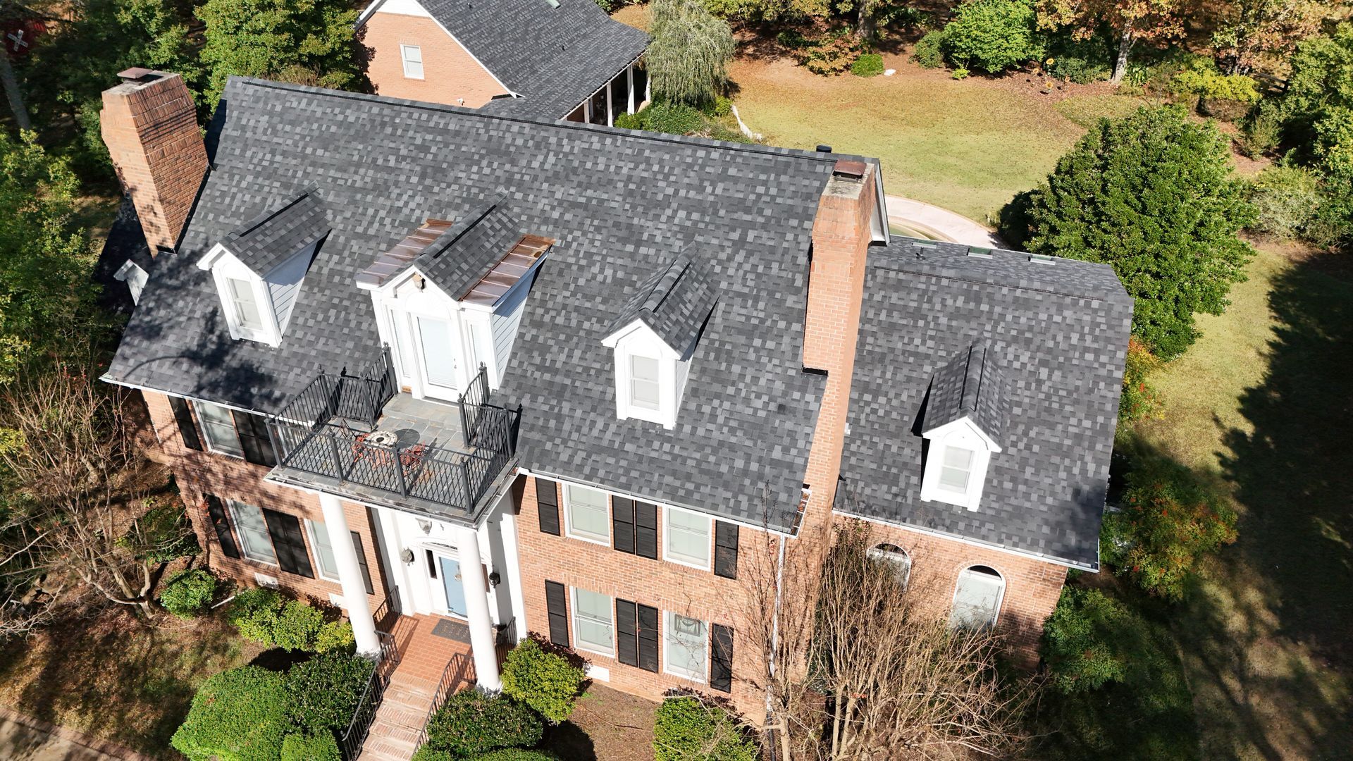 An aerial view of a large brick house with a black roof surrounded by trees.
